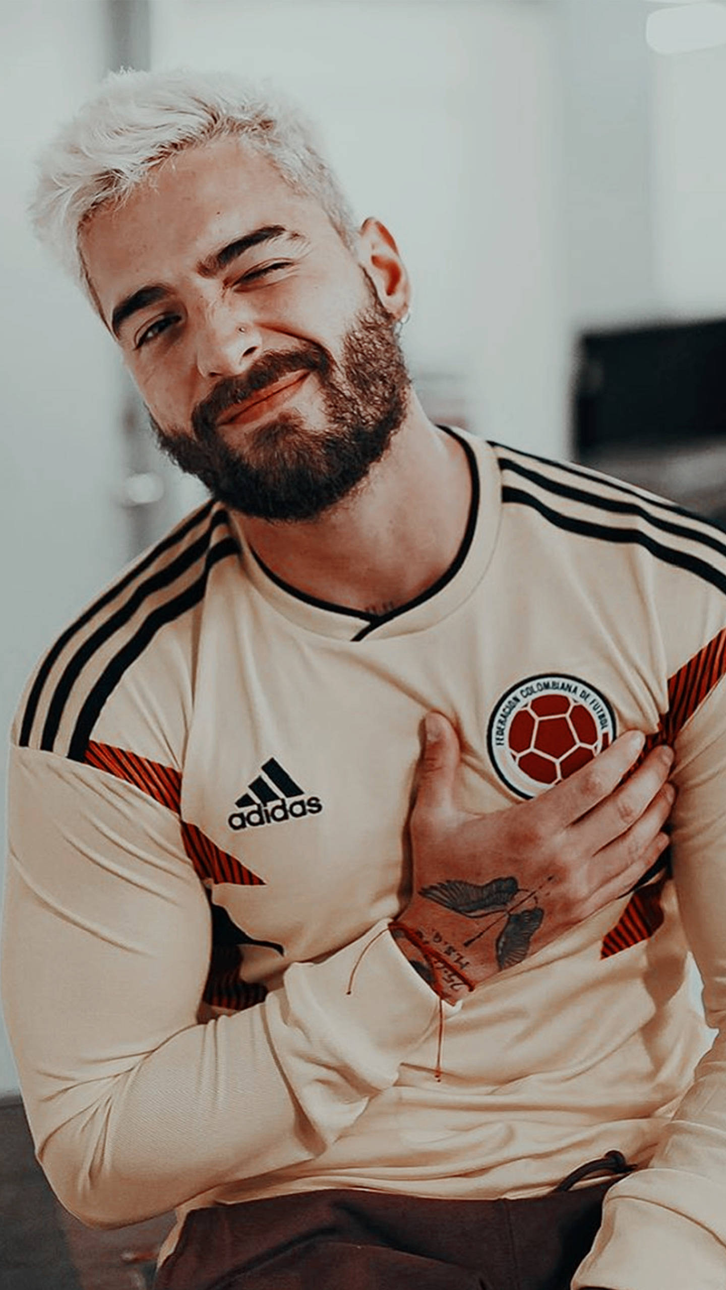Maluma 桌布 壁紙 — 一位微笑的白髮白鬍鬚男子身穿哥倫比亞足球球衣，將手放在心口上。