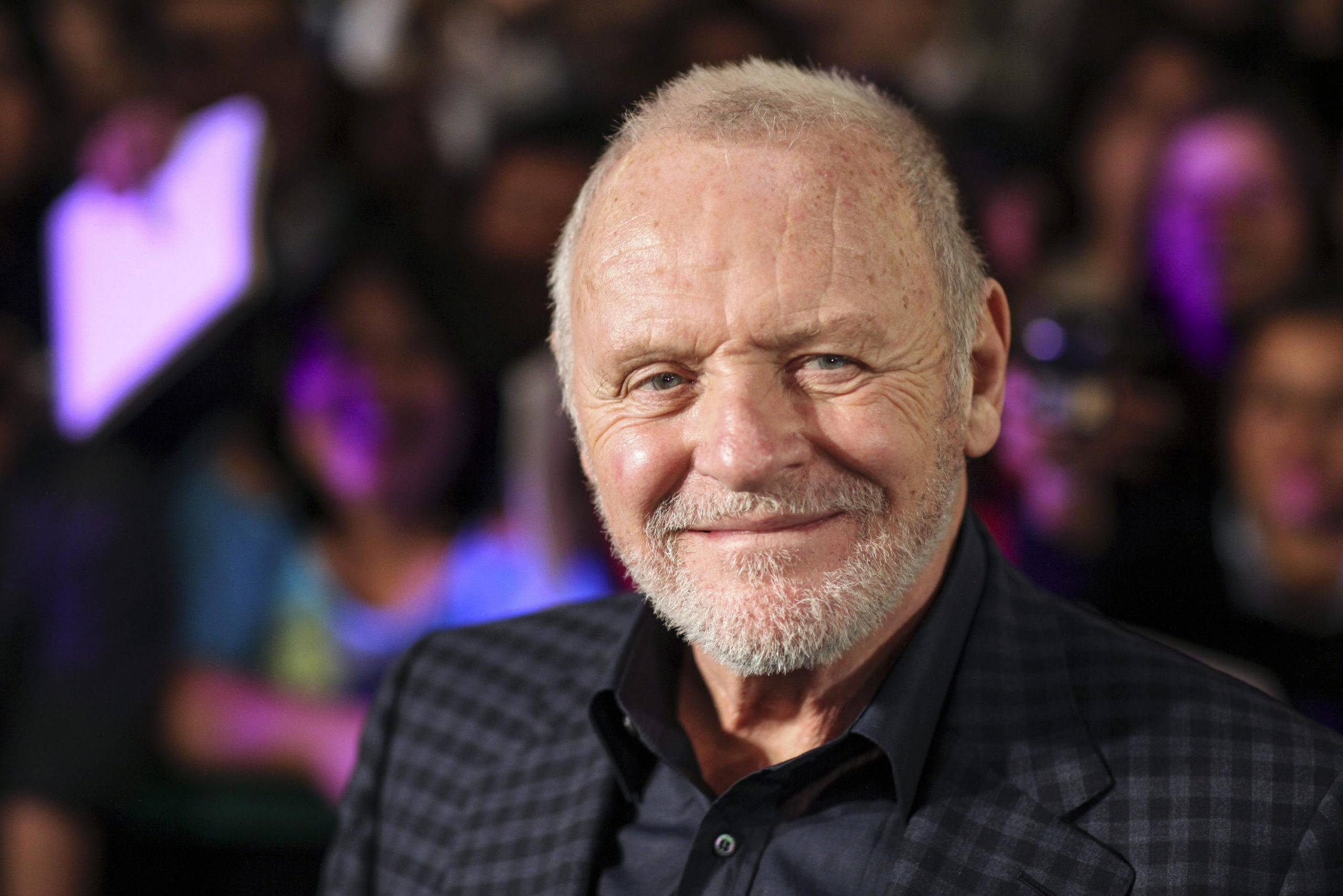 actor 桌布 壁紙 — 一位微笑的白髮白鬍鬚老年男子穿著格紋西裝外套，背景是模糊的人群和紫色燈光的特寫肖像。
