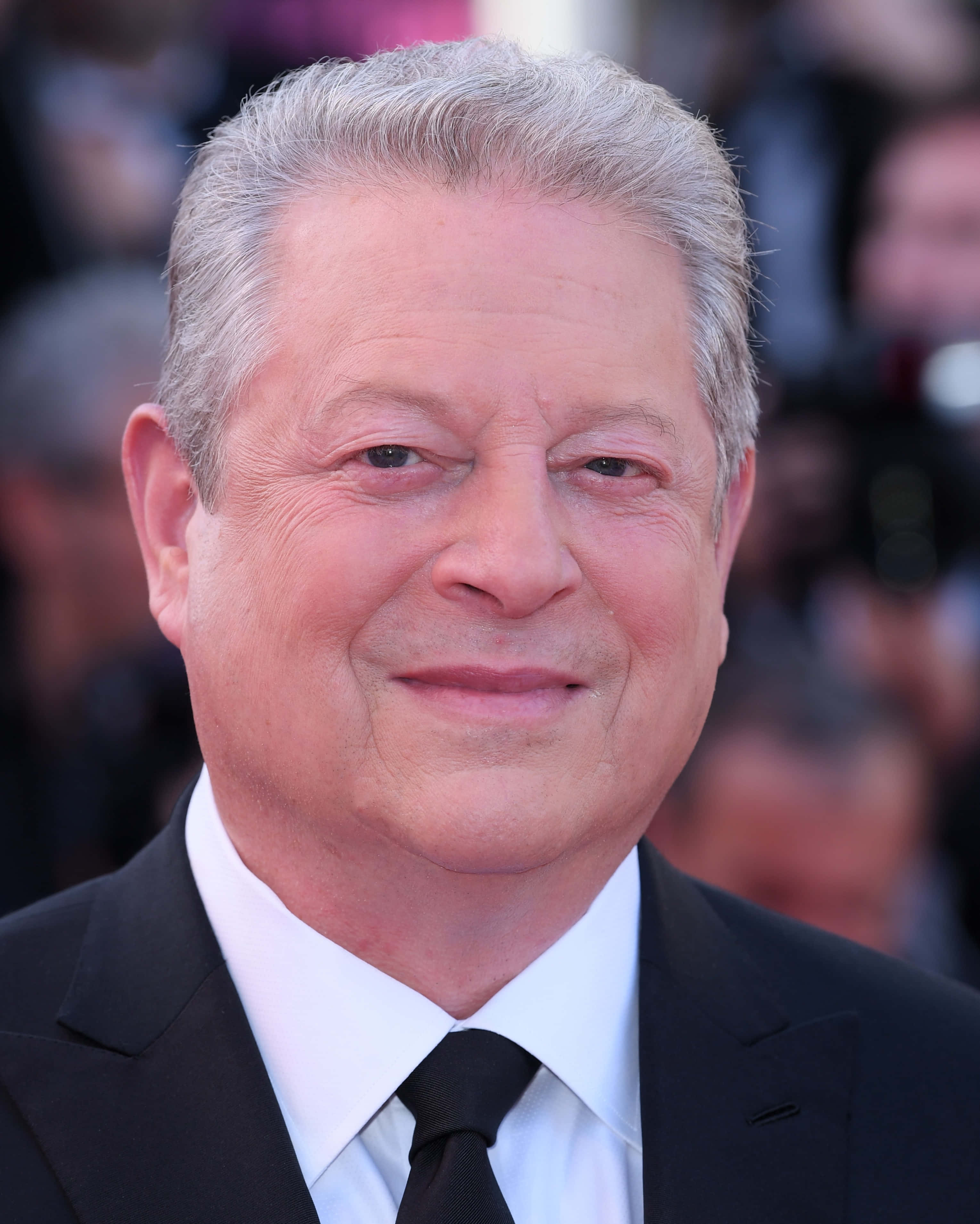 Celebrity 桌布 壁紙 — 一位微笑的白髮老年男子穿著黑色西裝和領帶，背景是模糊的人群的特寫肖像。