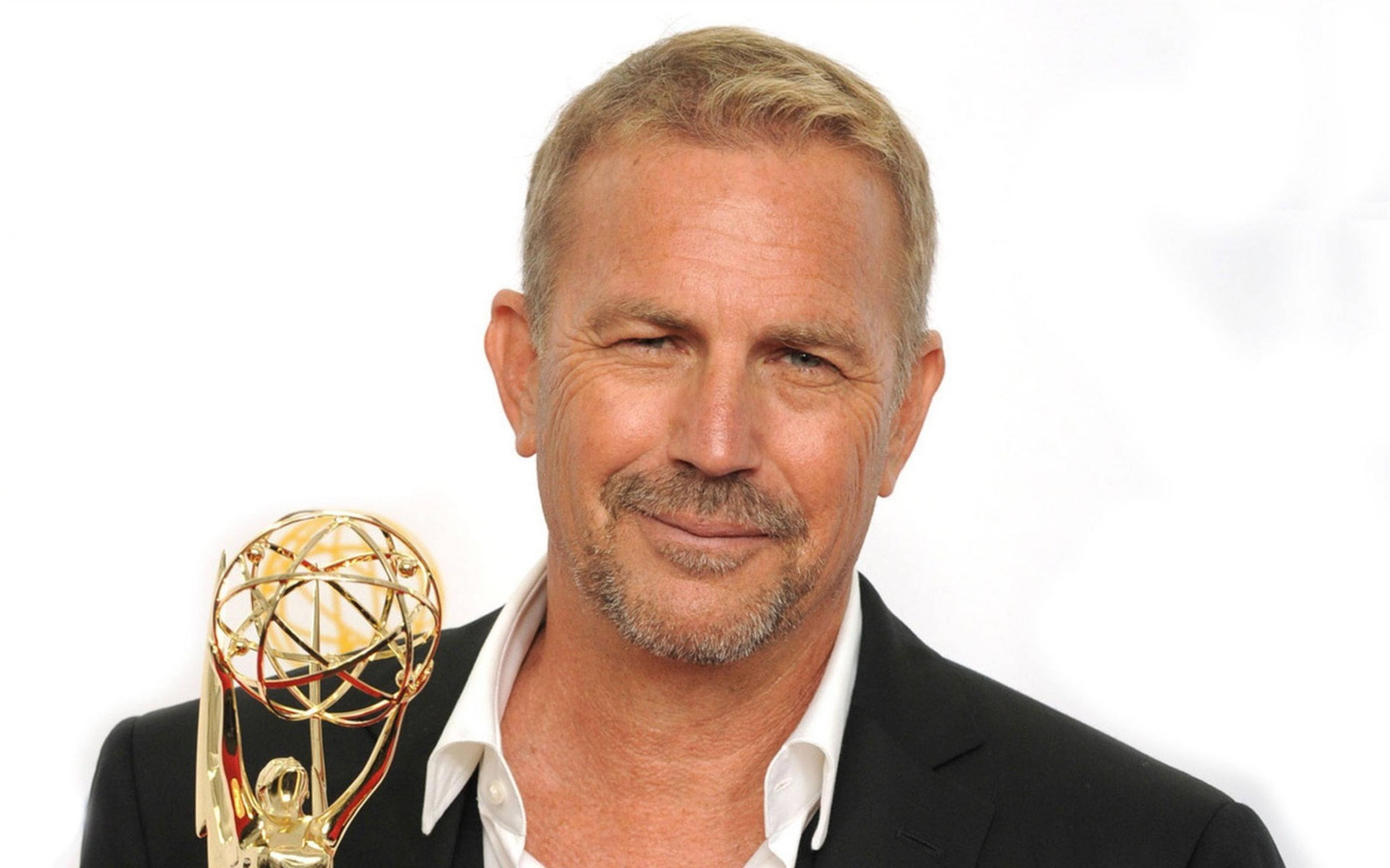 Kevin Costner 桌布 壁紙 — 一位微笑的白髮鬍鬚男士在白色背景前手持金色艾美獎獎座。