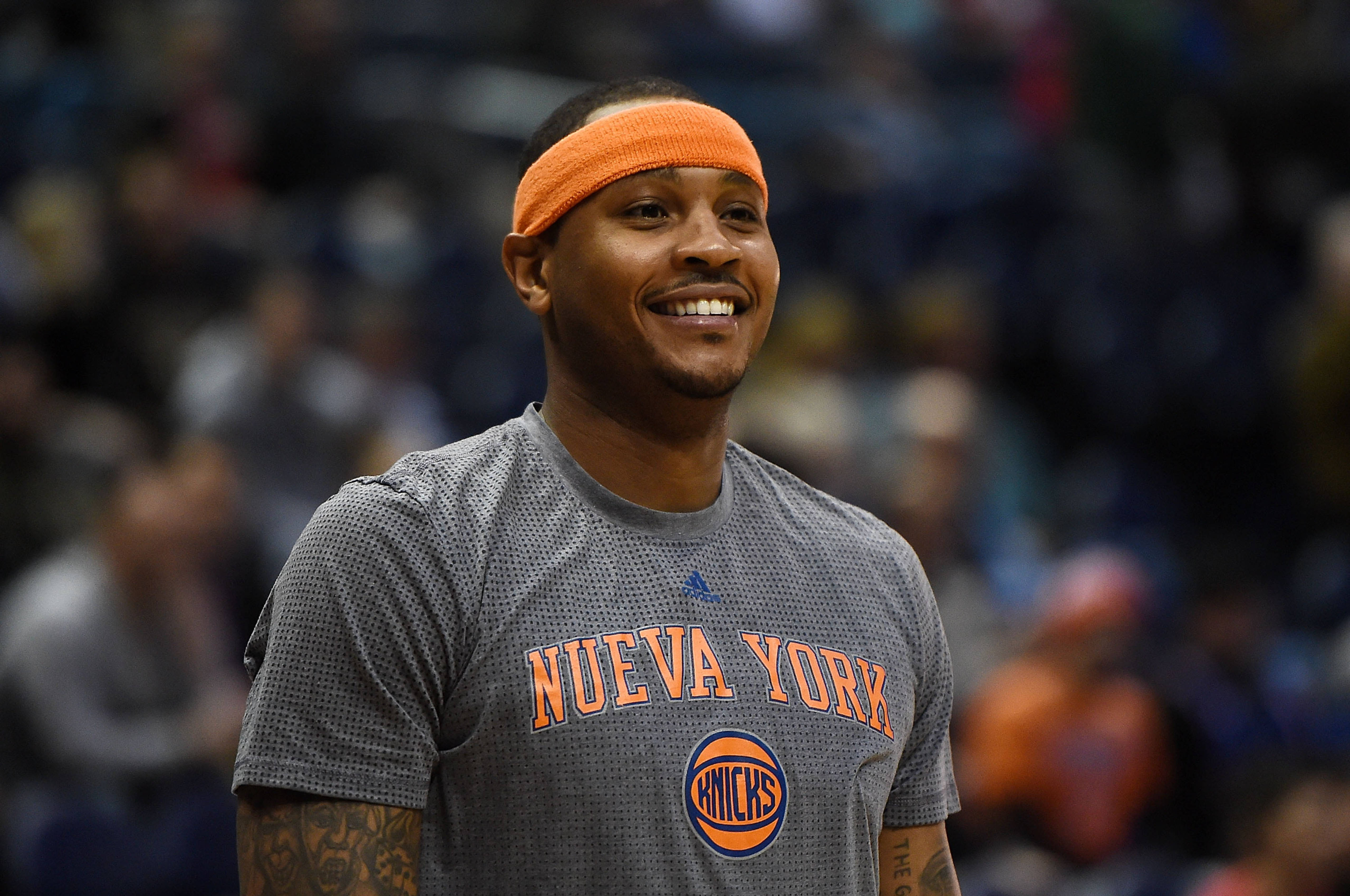 Carmelo 桌布 壁紙 — 一位微笑的籃球運動員戴著橙色頭帶，身穿「NUEVA YORK」球衣，站在擁擠的球場上。