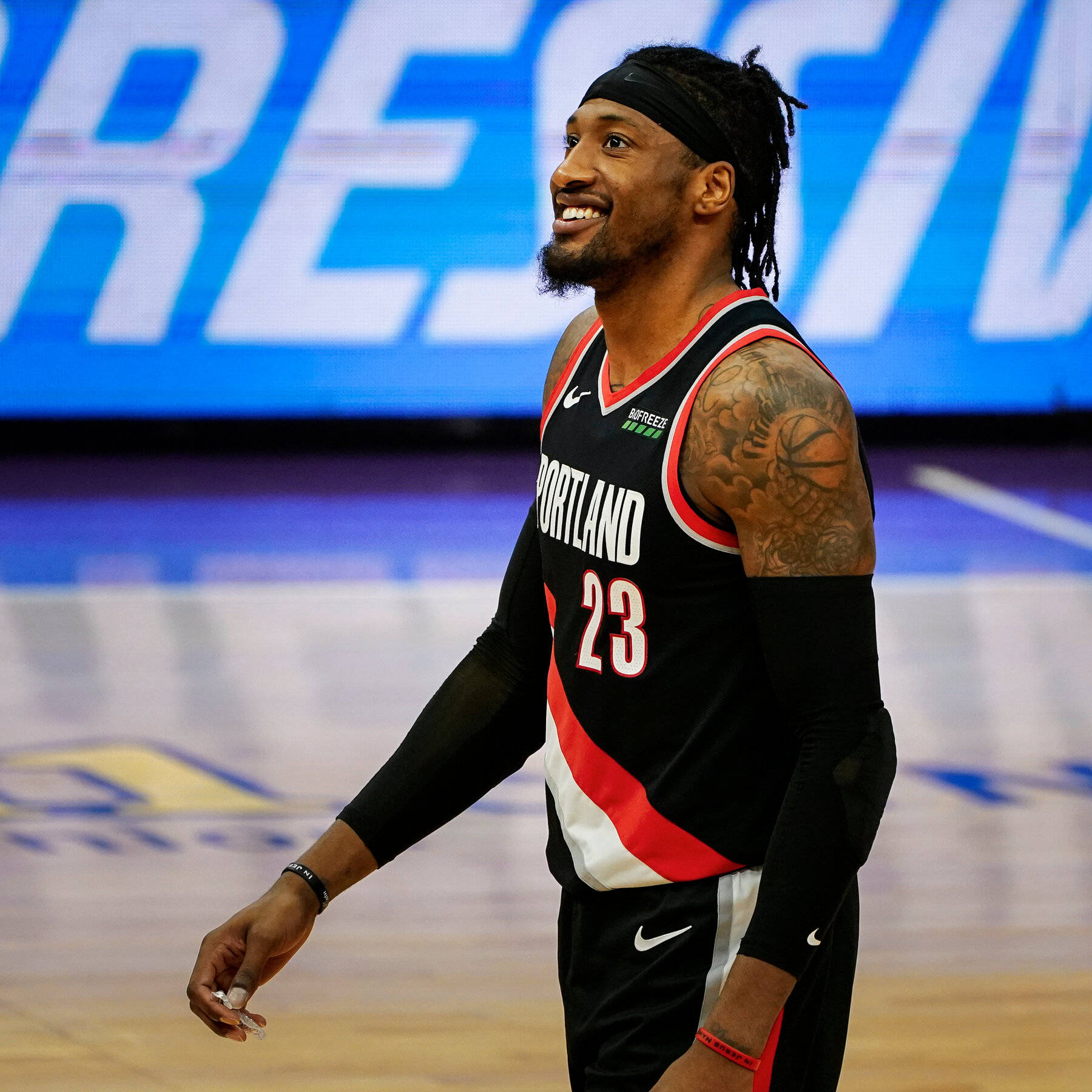 robert covington 桌布 壁紙 — 一位微笑的籃球運動員穿著波特蘭拓荒者隊球衣，在球場上行走，手臂有刺青並戴著頭帶。