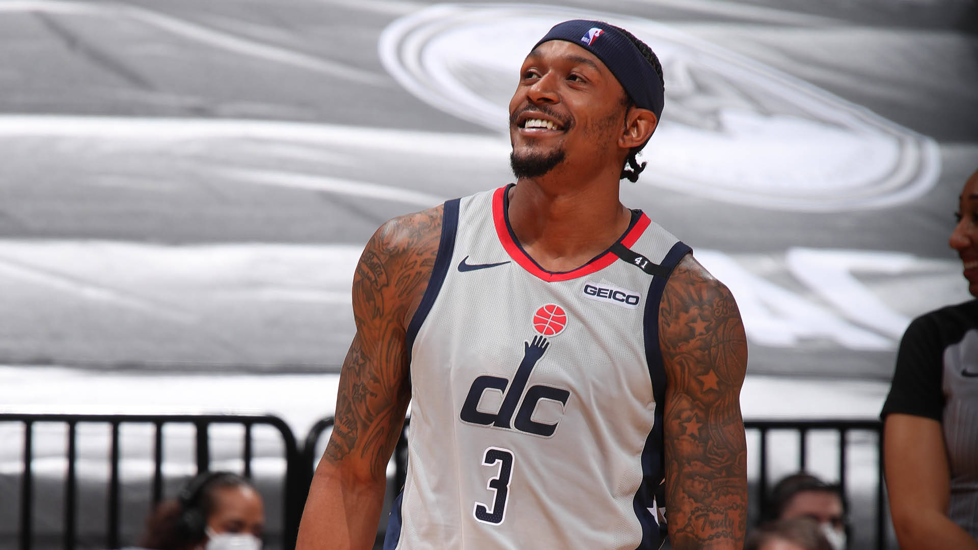 Bradley Beal 桌布 壁紙 — 一位微笑的籃球運動員身穿DC球衣，手臂上有刺青，自信地站在球場上。