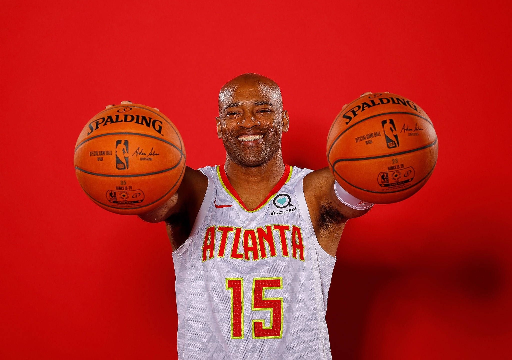NBA 桌布 壁紙 — 一位微笑的籃球運動員身穿亞特蘭大球衣，在鮮紅色的工作室背景前拿著兩個Spalding籃球。