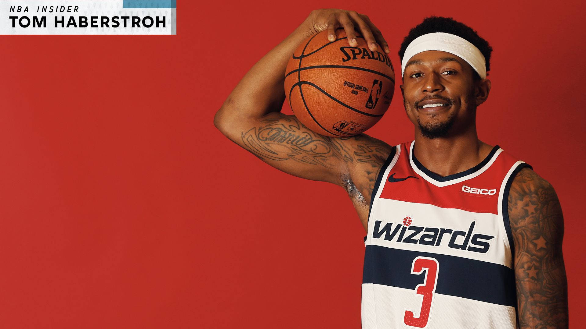 Bradley Beal 桌布 壁紙 — 一位微笑的籃球運動員身穿巫師隊球衣，在純紅色背景前拿著一個Spalding籃球。