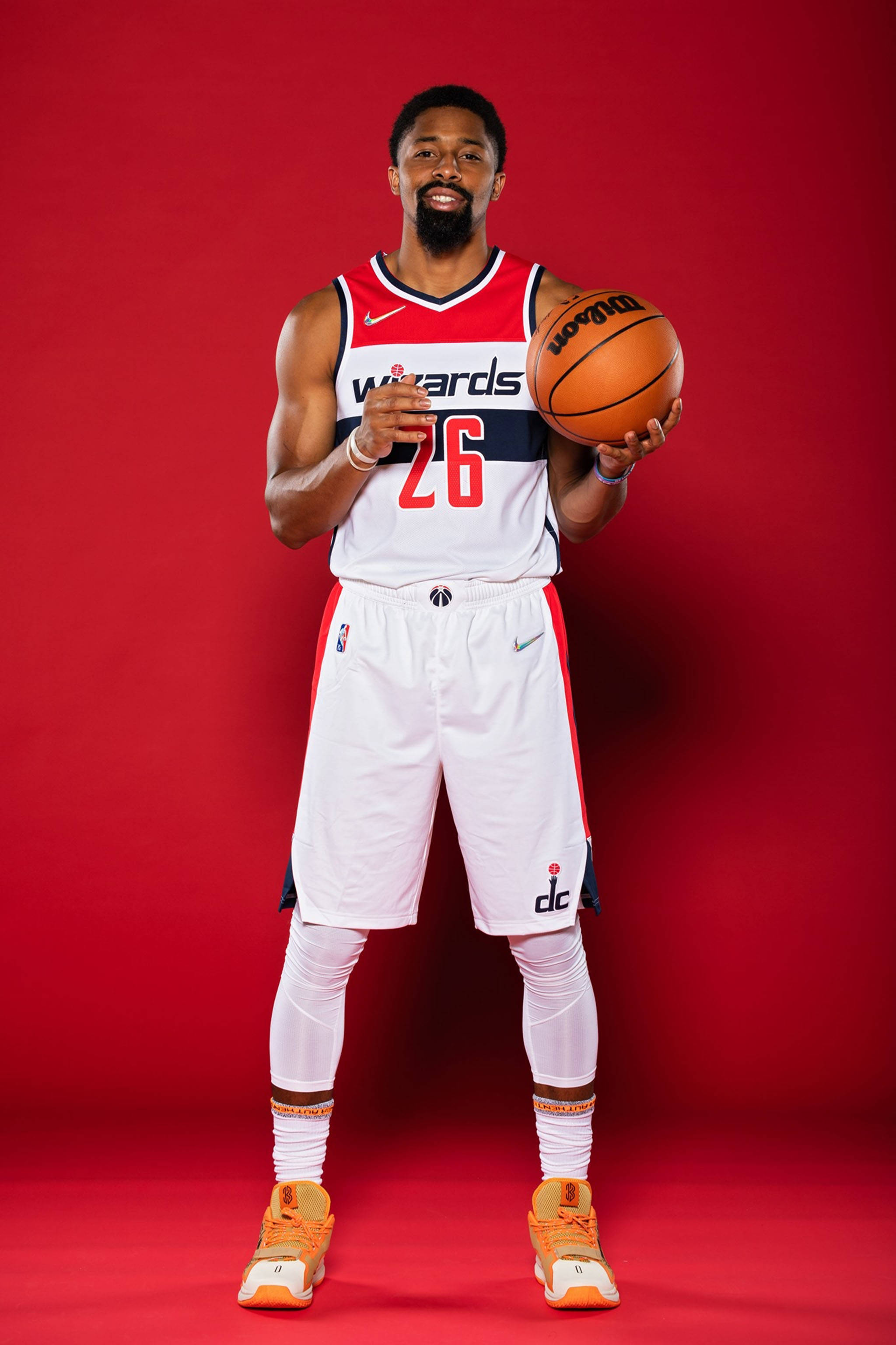 spencer dinwiddie 桌布 壁紙 — 一位微笑的籃球運動員身穿巫師隊球衣，在純紅色攝影棚背景前持球。