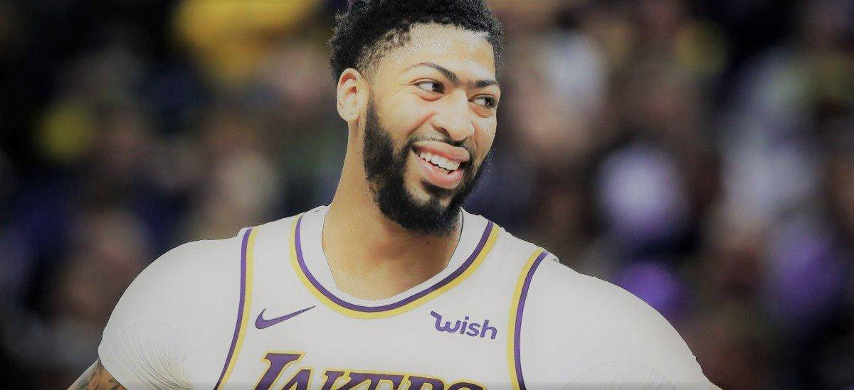 Anthony Davis 桌布 壁紙 — 一位微笑的籃球運動員身穿帶有紫色飾邊的白色湖人隊球衣，自信地站在模糊的人群背景前。