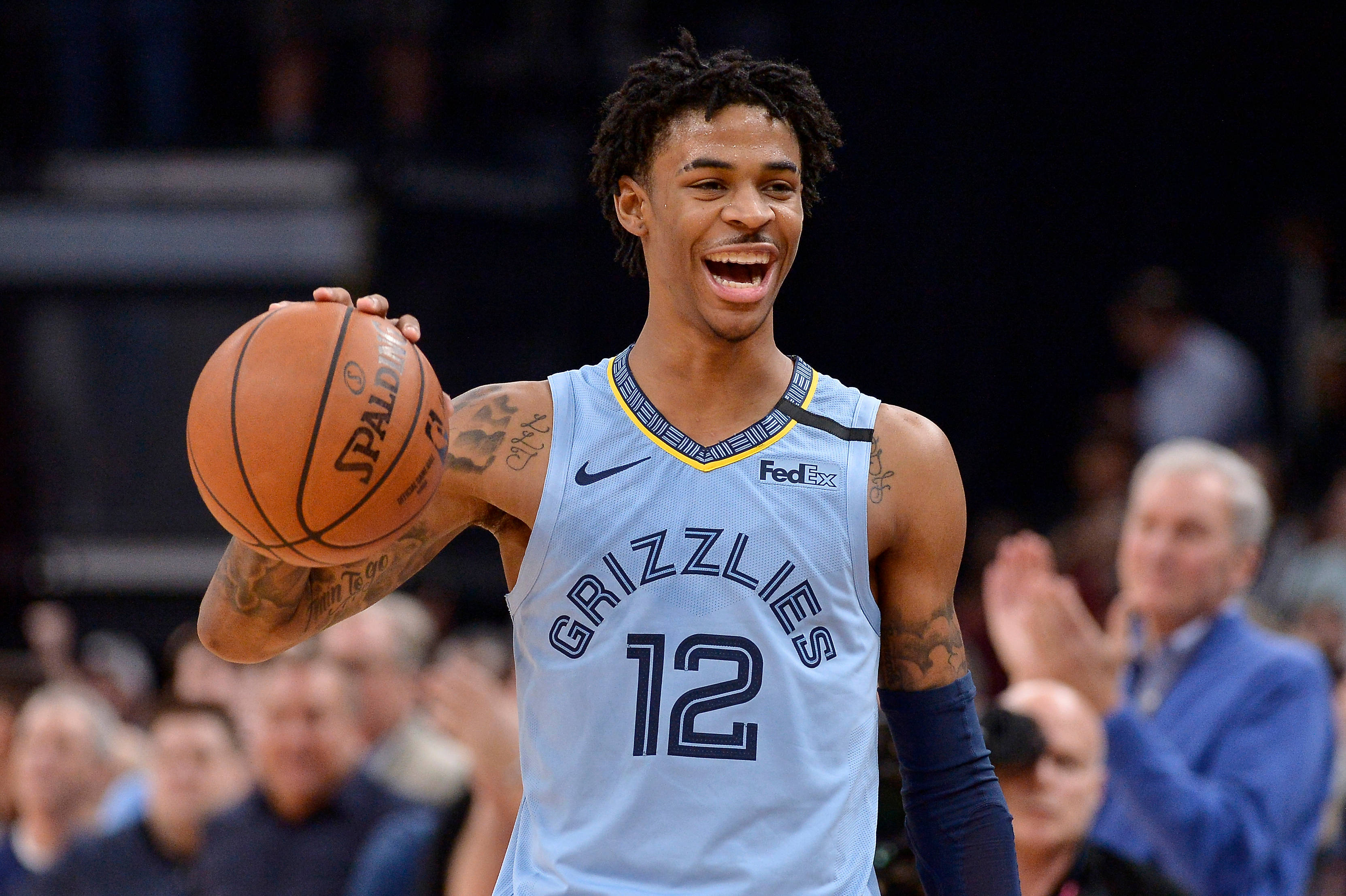 Grizzlies 桌布 壁紙 — 一位微笑的籃球運動員身穿淺藍色灰熊隊球衣，手持Spalding籃球，背景中球迷歡呼。