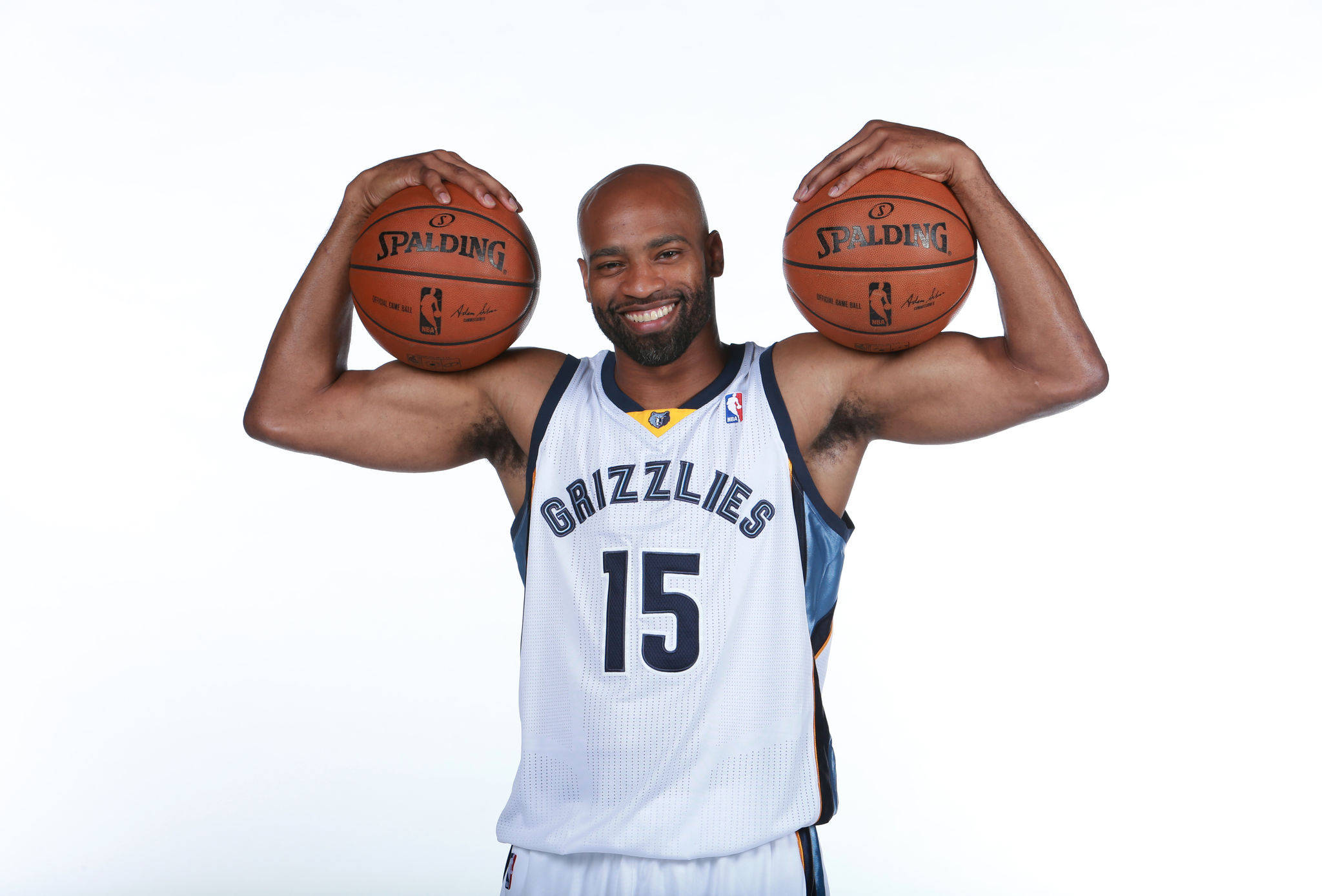NBA 桌布 壁紙 — 一位微笑的籃球運動員身穿灰熊隊球衣，在純白色背景上將兩個 Spalding 籃球舉過肩膀。