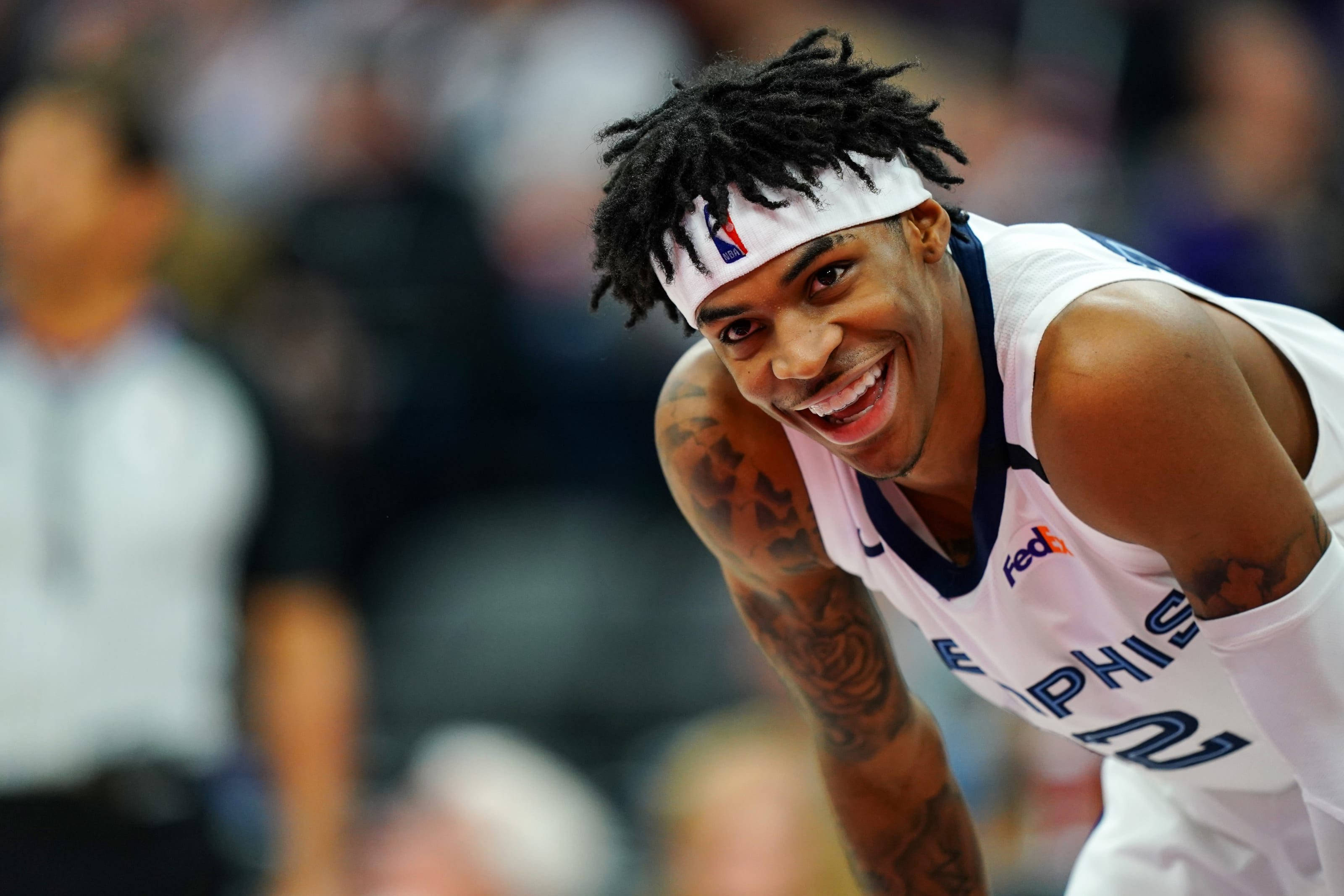 Grizzlies 桌布 壁紙 — 一位微笑的籃球運動員身穿白色曼菲斯球衣，向前傾斜，手臂上的刺青清晰可見。