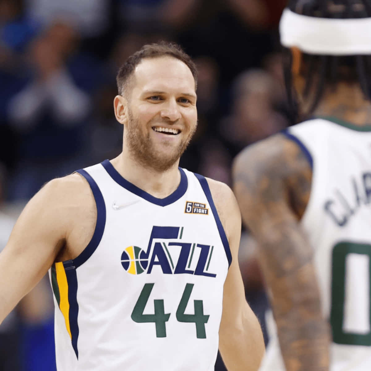 NBA 桌布 壁紙 — 一位微笑的籃球運動員身穿白色爵士隊44號球衣，在明亮的場館燈光下於比賽中慶祝。