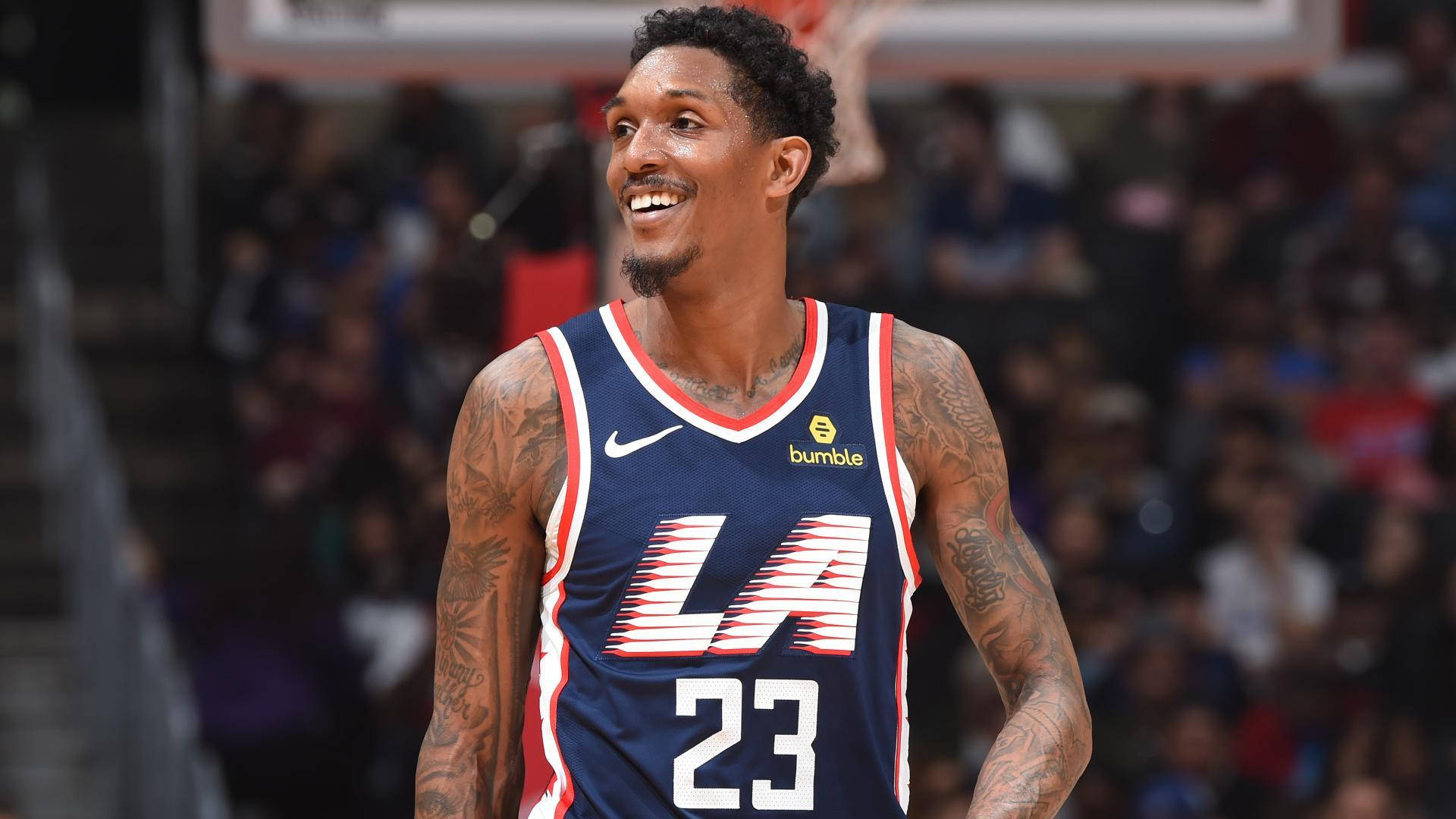 Lou Williams 桌布 壁紙 — 一位微笑的籃球運動員身穿藍色LA球衣，號碼23，站在球場上，背景是模糊的觀眾。