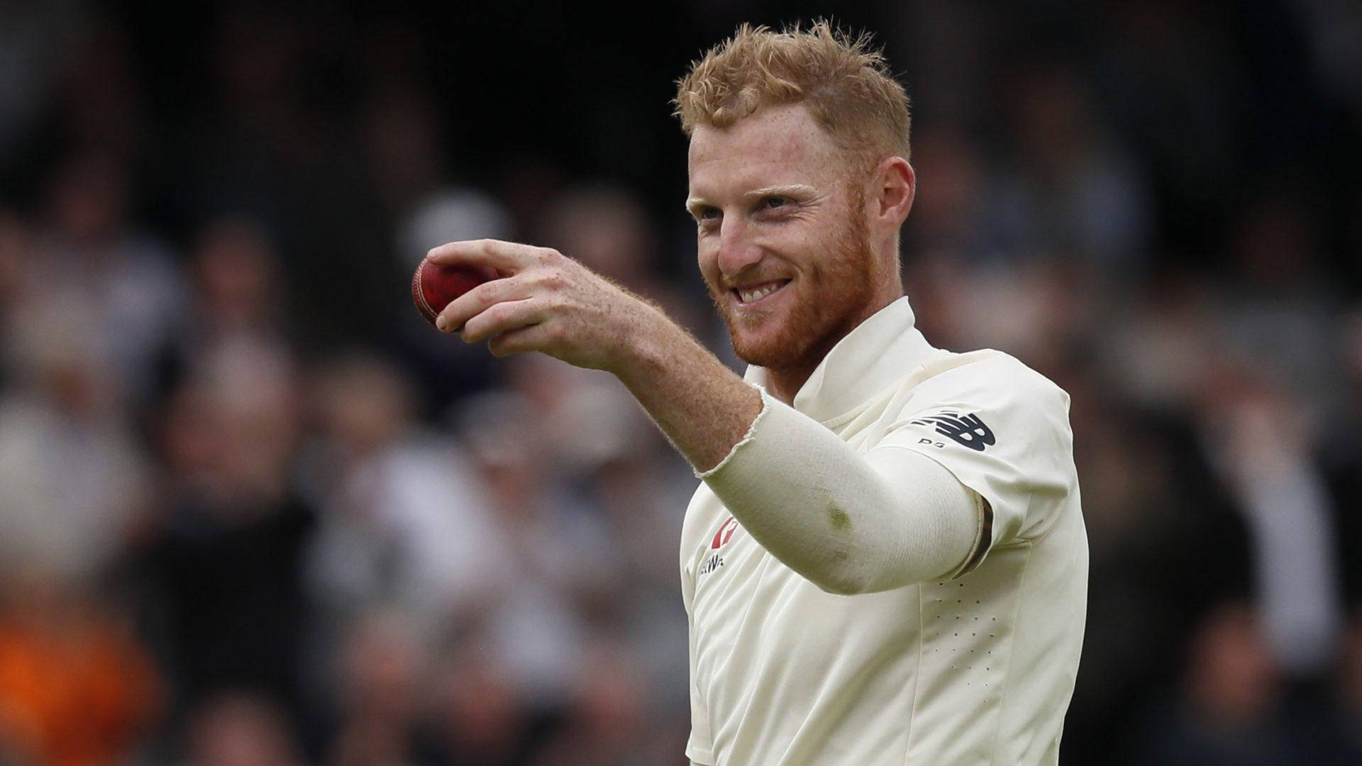 Ben Stokes 桌布 壁紙 — 一位微笑的紅髮板球運動員身穿白色制服，在模糊的人群中手持紅色球進行動作。