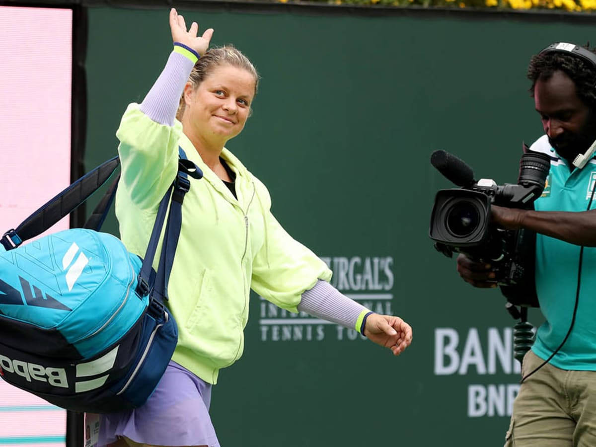 Woman 桌布 壁紙 — 一位微笑的網球選手向粉絲揮手，同時背著一個藍色 Babolat 袋，攝影師在綠色球場背景下拍攝她。