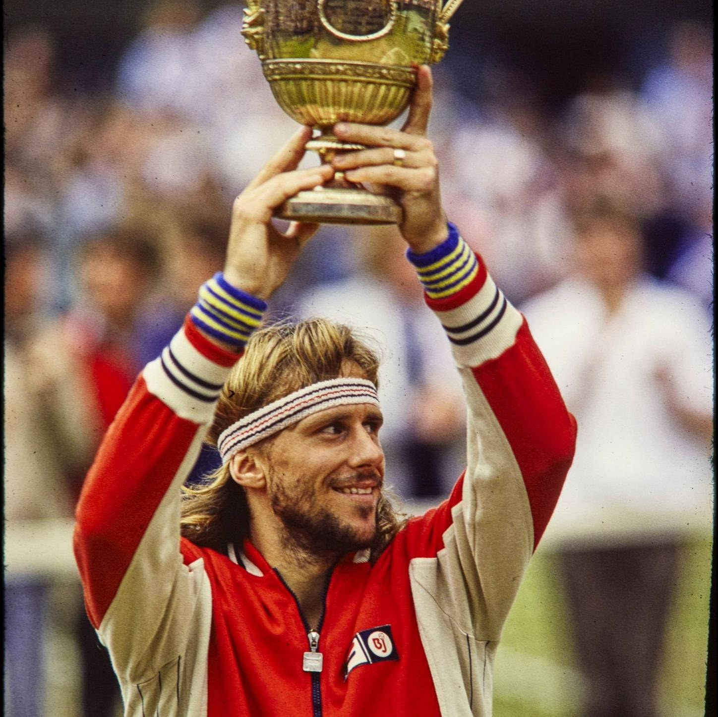 運動 桌布 壁紙 — 一位微笑的網球選手身穿紅米色外套，雙手將金色獎盃高舉過頭頂。