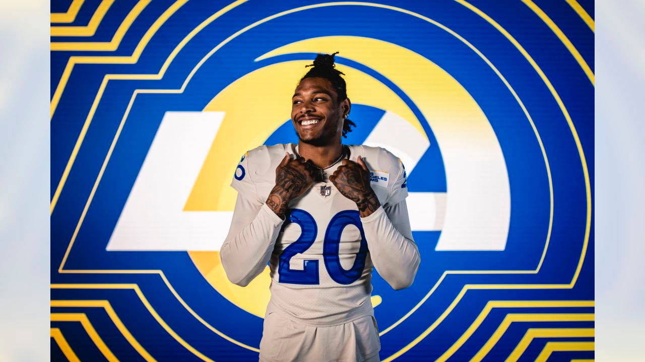 Ramsey 桌布 壁紙 — 一位微笑的美式足球員身穿白色球衣，號碼20，在鮮明的藍黃色LA Rams標誌背景前自信地擺姿勢。
