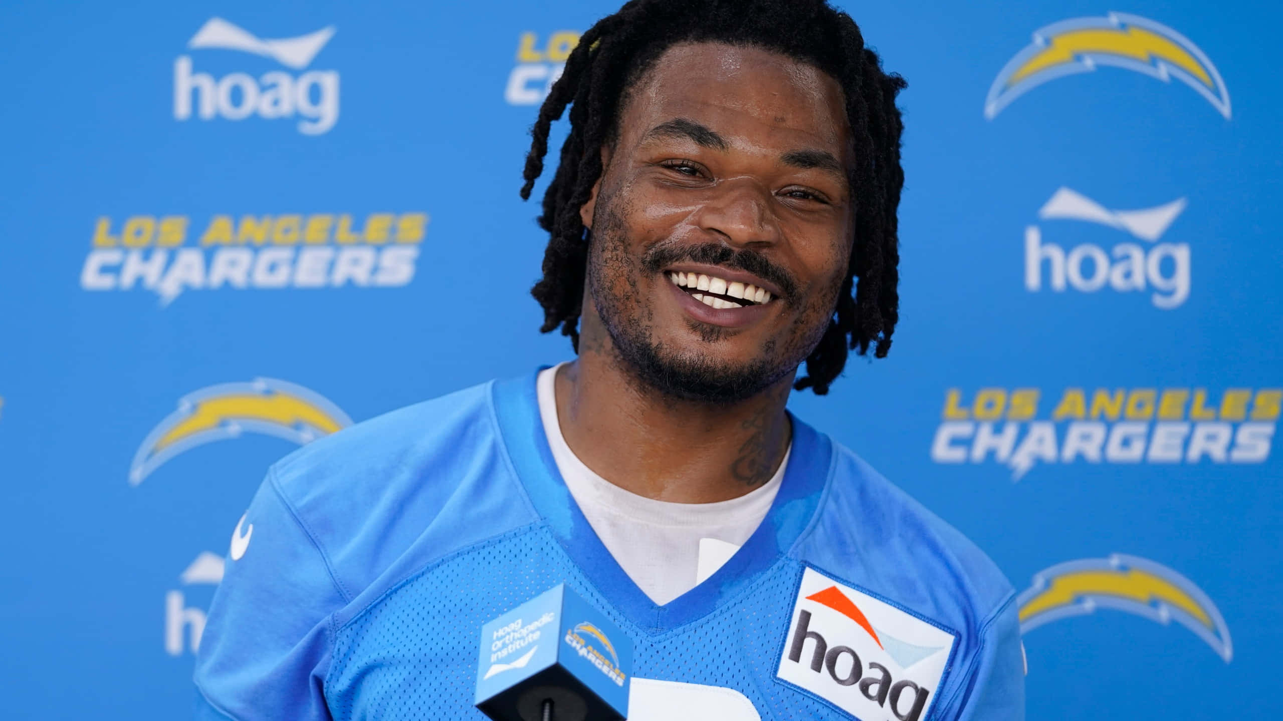 NFL 桌布 壁紙 — 一位微笑的美式足球員身穿藍色洛杉磯電光隊球衣，站在品牌藍色背景前。
