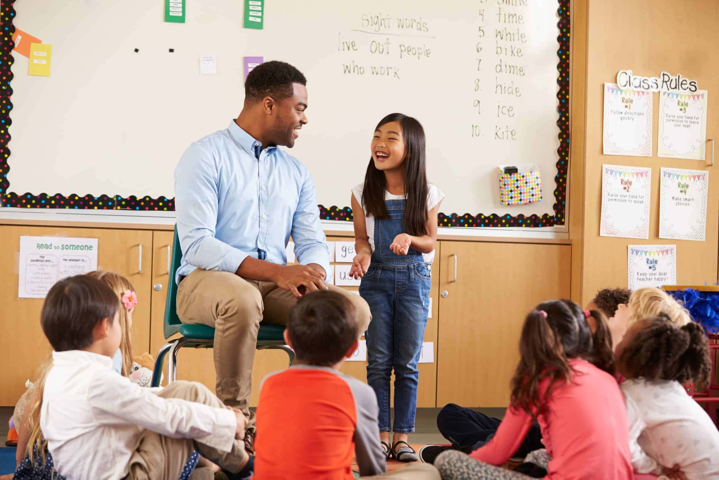 Classroom 桌布 壁紙 — 一位微笑的老師在教室圓圈中與一位快樂的學生互動，周圍是專注的孩子們。