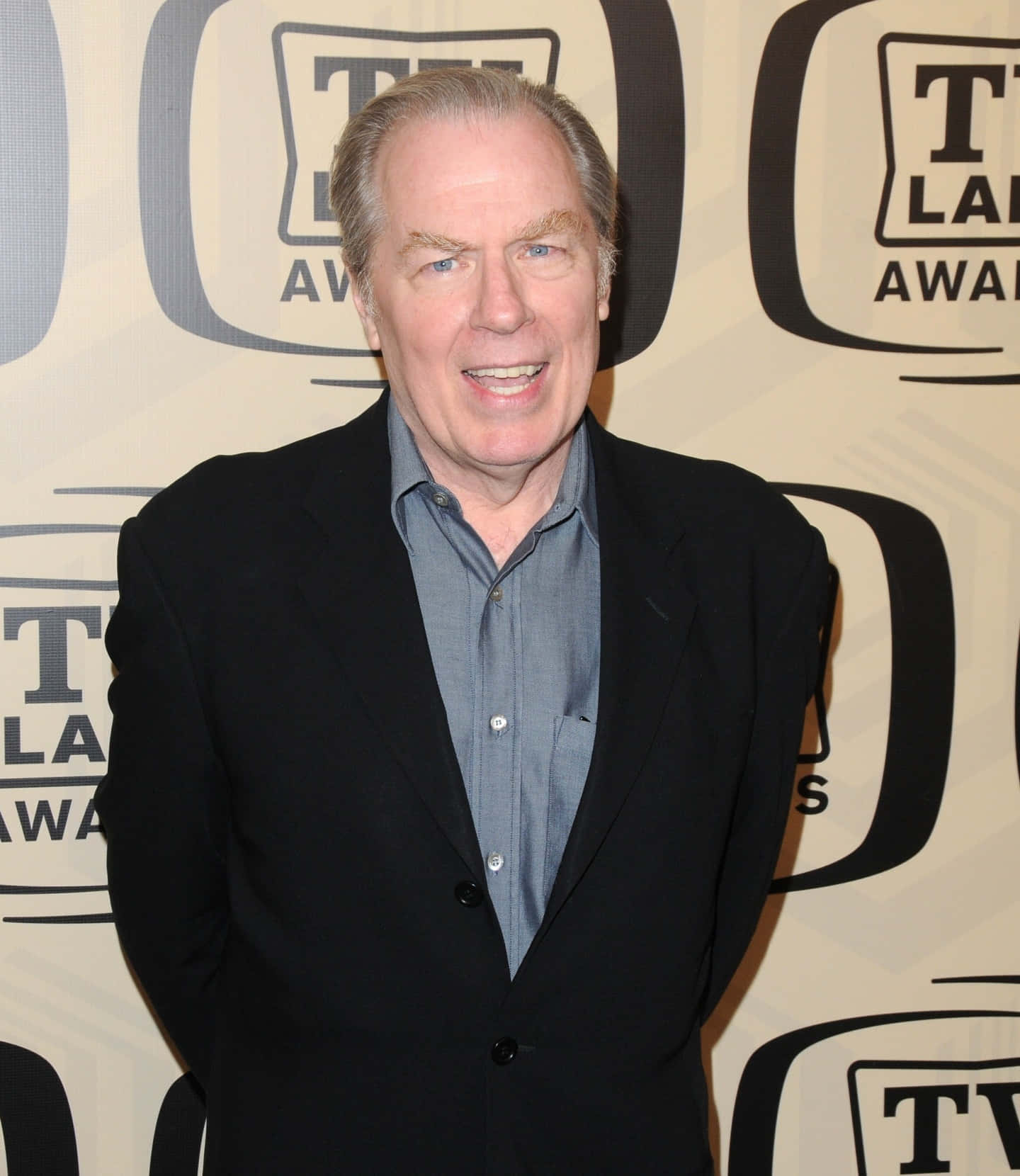 Michael Mckean 桌布 壁紙 — 一位微笑的老年男士身穿黑色西裝和藍色襯衫，自信地站在帶有品牌背景的TV Land Awards活動中。