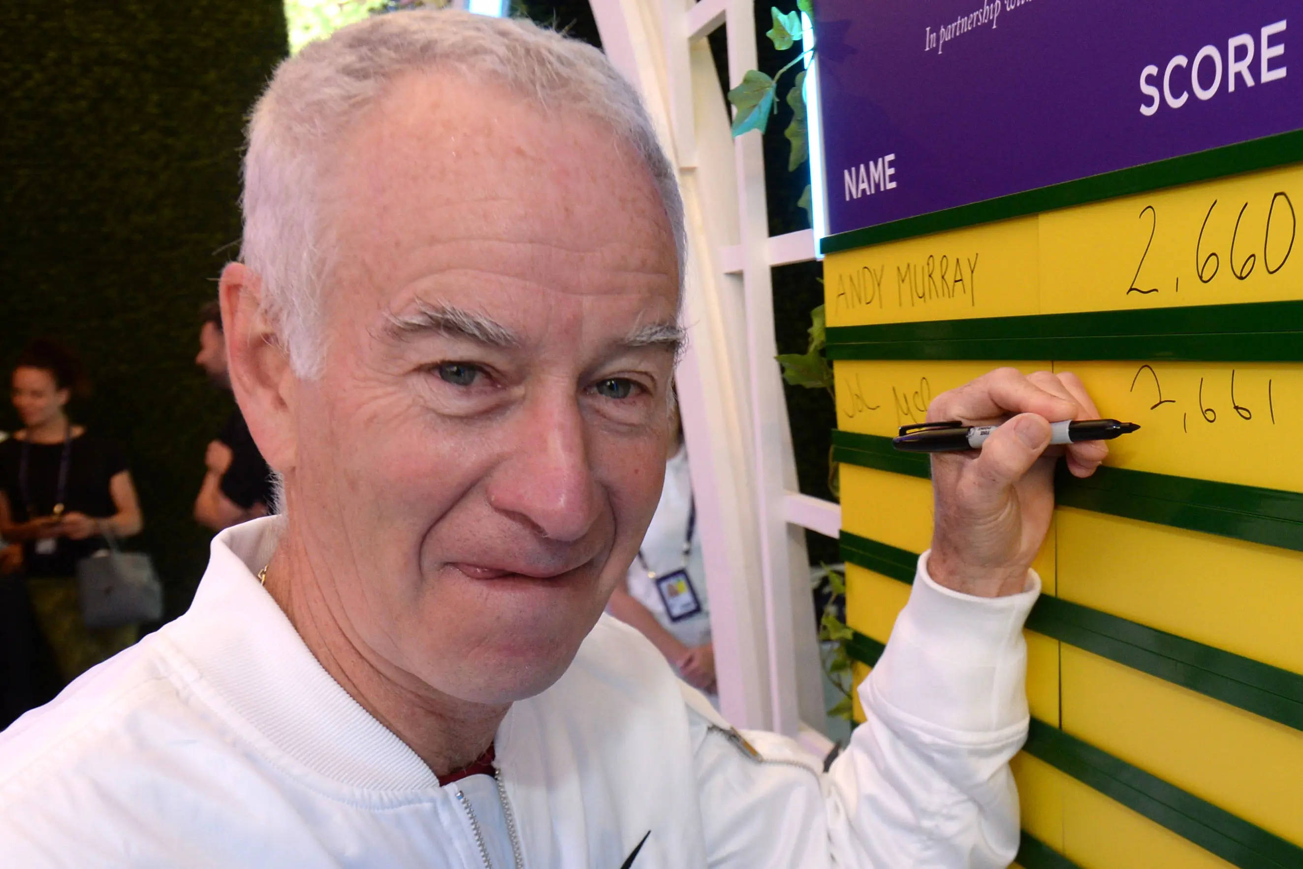 Tennis 桌布 壁紙 — 一位微笑的老年男子穿著白色外套，在活動中將自己的分數寫在黃綠色的記分板上。