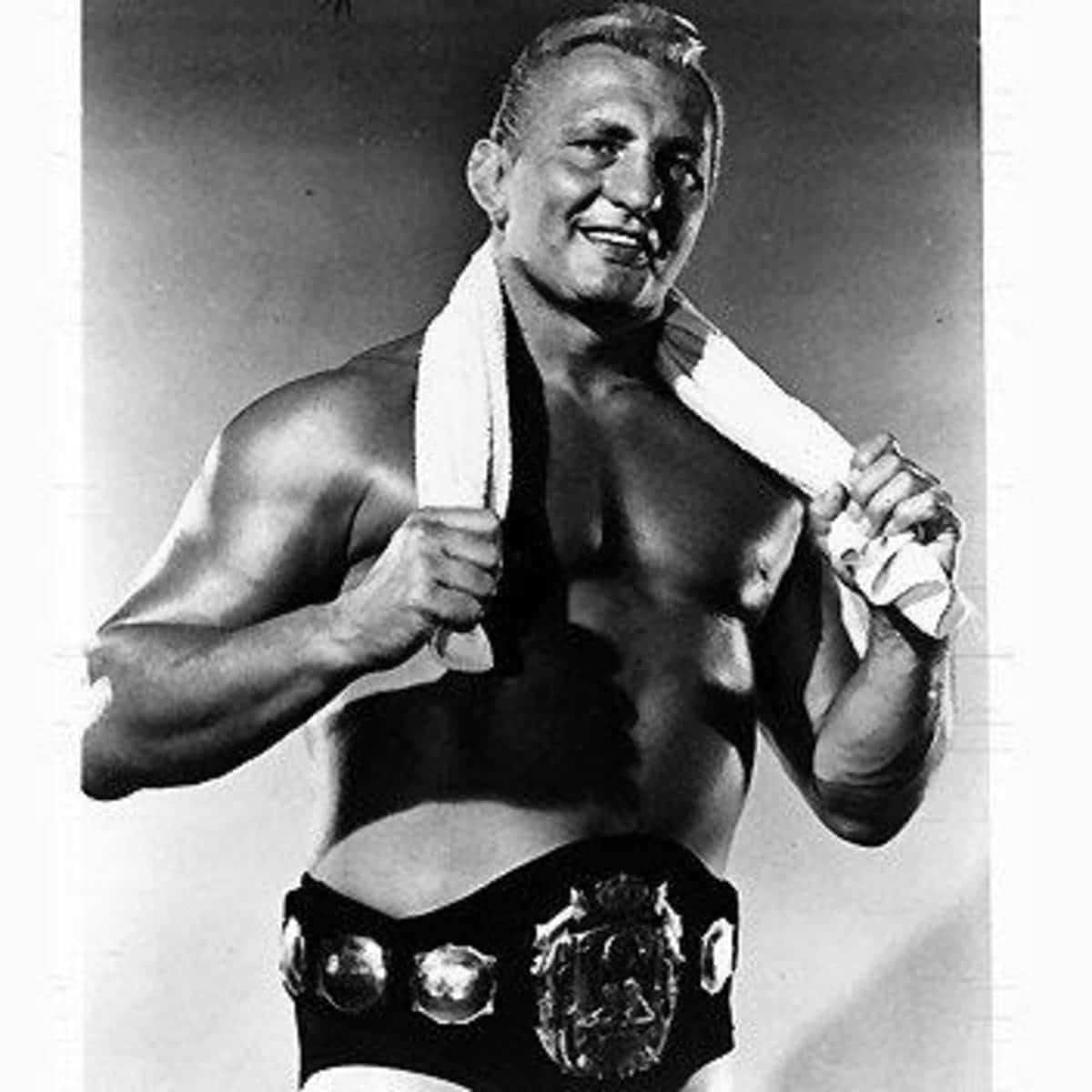 WWE 桌布 壁紙 — 一位微笑的肌肉摔角手，黑白風格，肩上披著毛巾，腰間繫著冠軍腰帶。