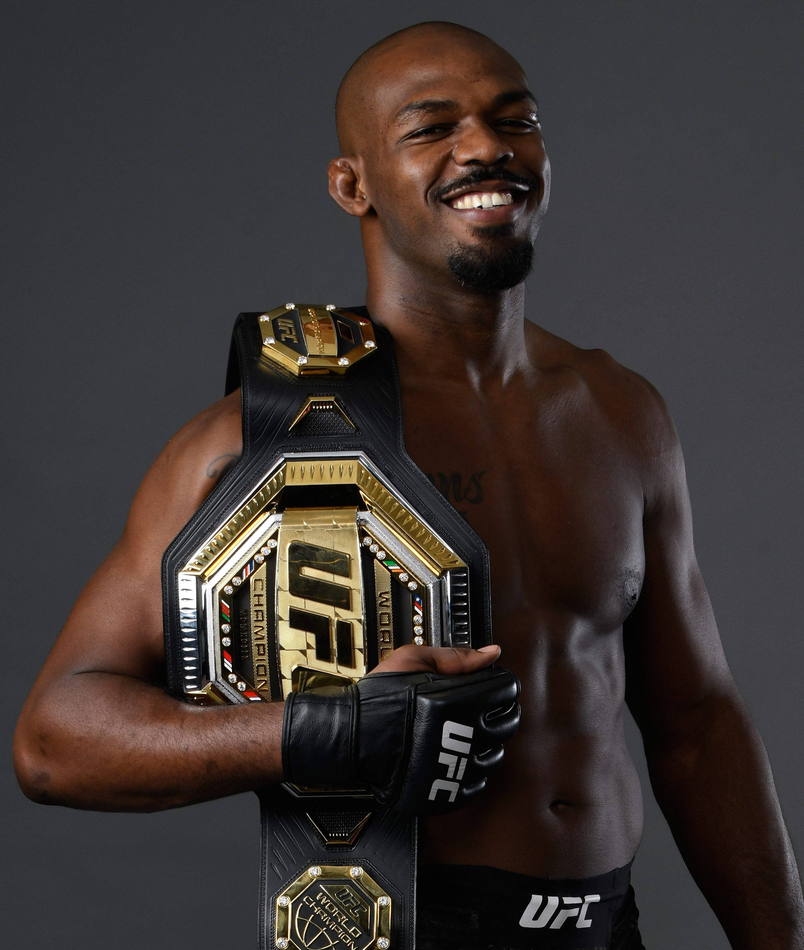 Champion 桌布 壁紙 — 一位微笑的肌肉發達戰士在黑暗的攝影棚背景下自豪地舉起閃亮的UFC冠軍腰帶。