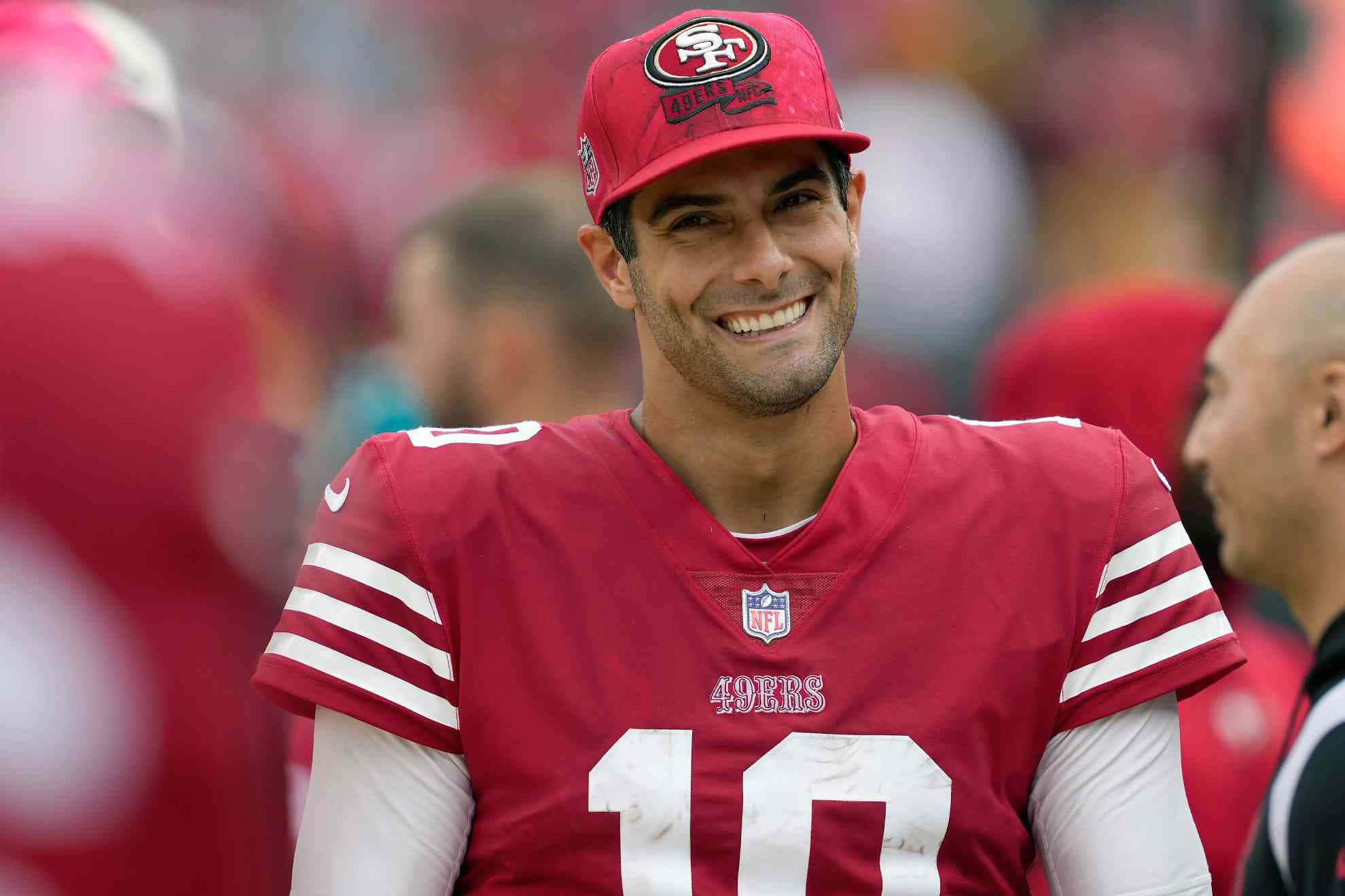 Jimmy Garoppolo 桌布 壁紙 — 一位微笑的舊金山49人隊四分衛，身穿紅色10號球衣，在陽光明媚的比賽日對著鏡頭綻放光芒。