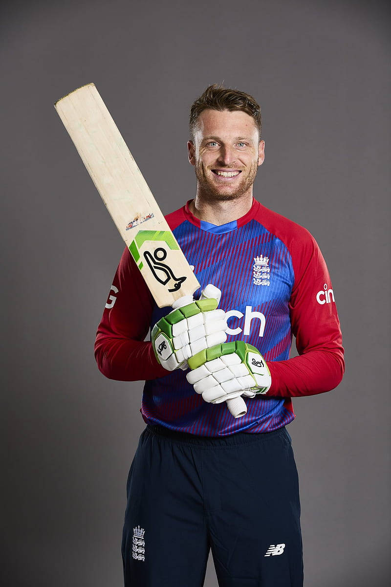 jos buttler 桌布 壁紙 — 一位微笑的英格蘭板球運動員穿著隊服，在純灰色工作室背景前拿著球棒和手套。