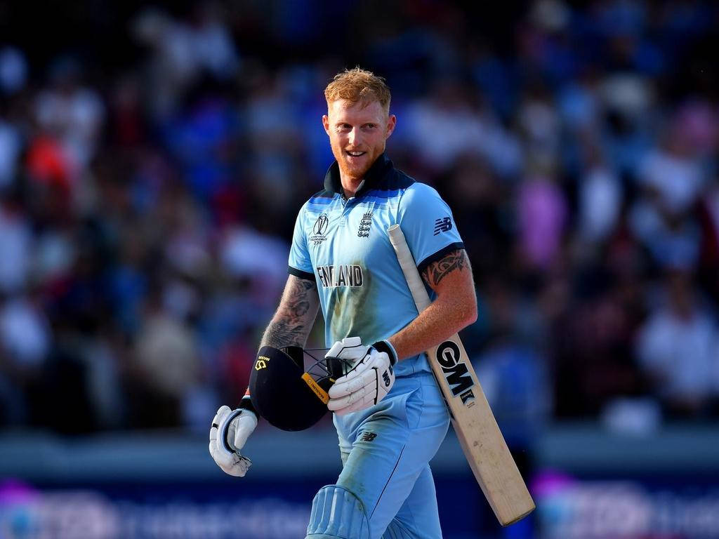 Ben Stokes 桌布 壁紙 — 一位微笑的英格蘭板球運動員身穿淺藍色制服，自信地拿著球棒和頭盔在擠滿人的體育場上行走。