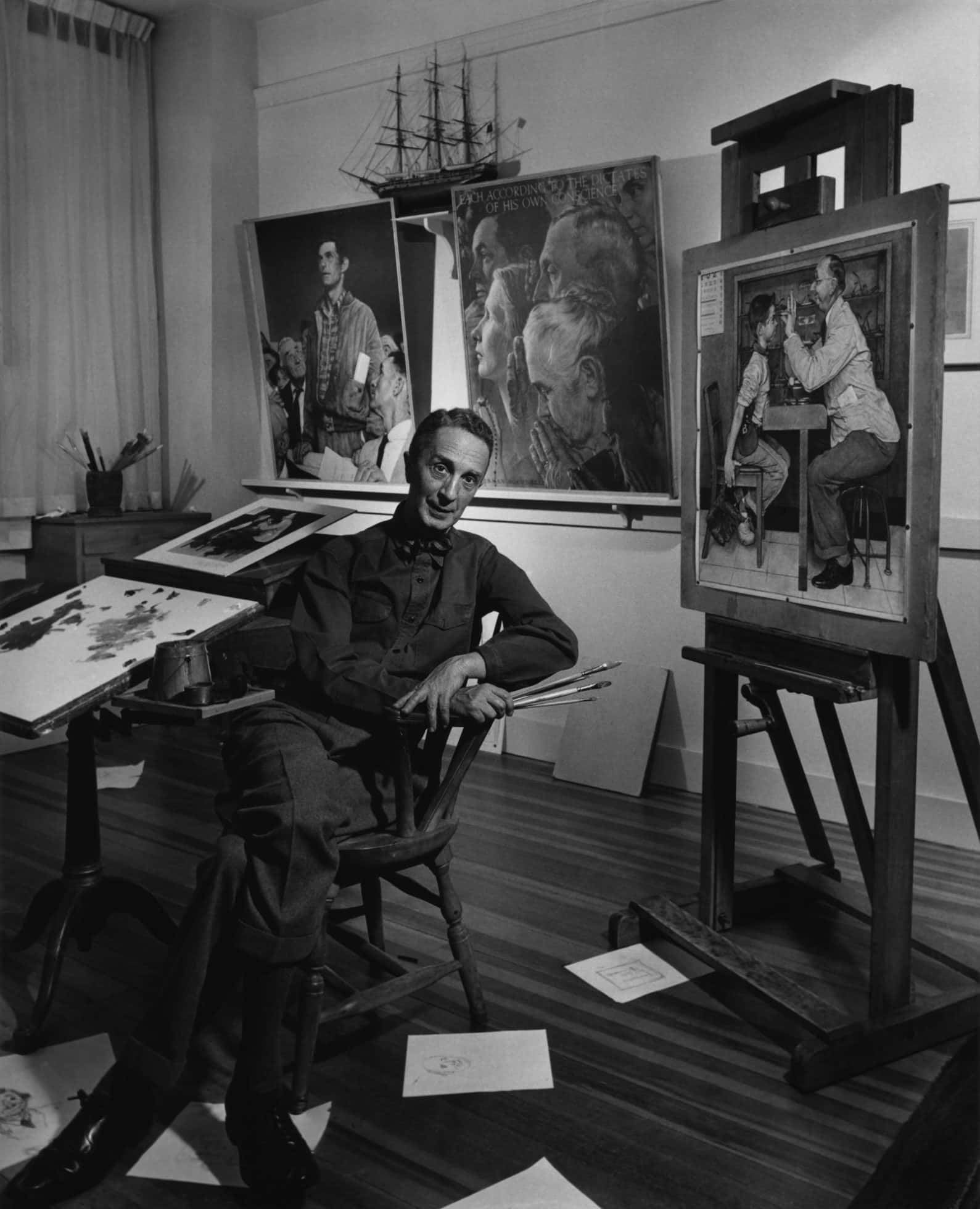 Norman Rockwell 桌布 壁紙 — 一位微笑的藝術家坐在他雜亂的工作室裡，周圍環繞著大型畫作和一個正在進行肖像畫的畫架。