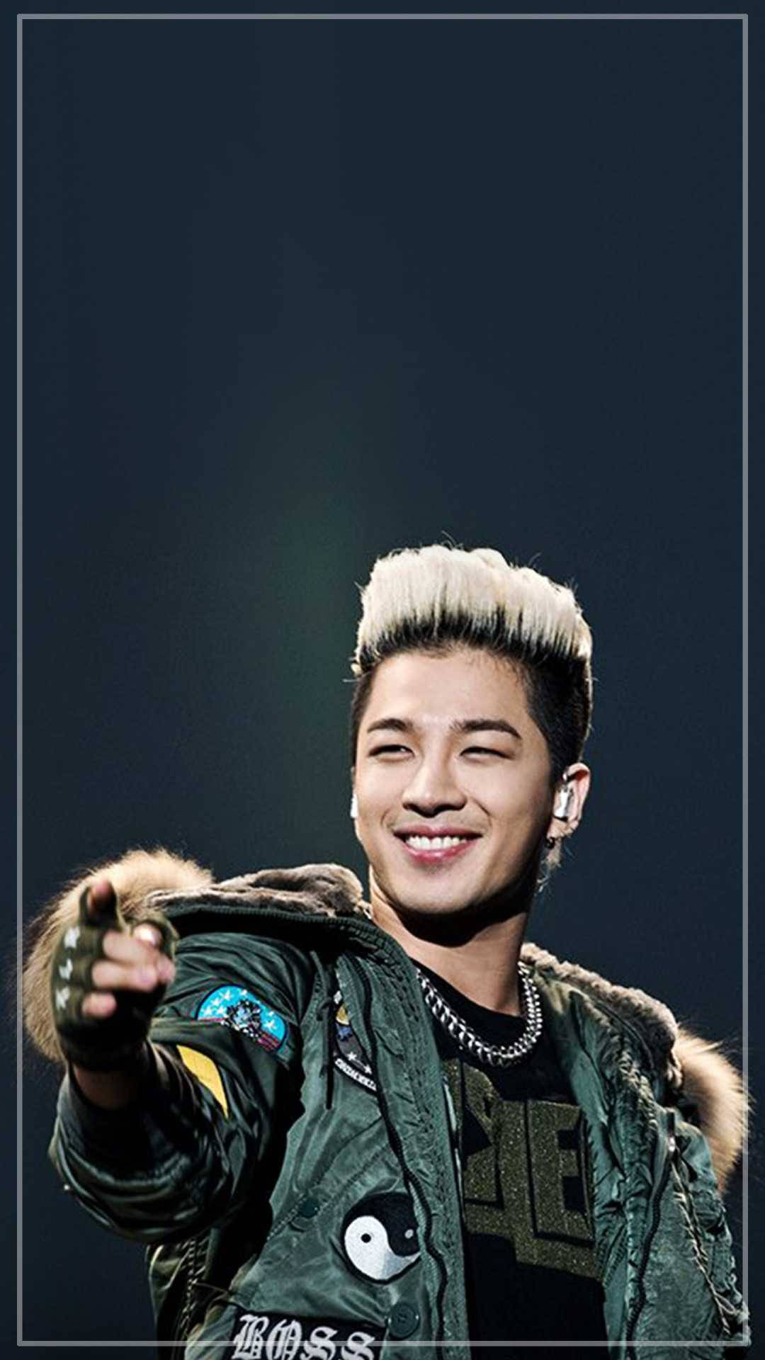 Bigbang 桌布 壁紙 — 一位微笑的表演者，漂染了頭髮，身穿綠色外套，在舞台燈光下直接指向觀眾。