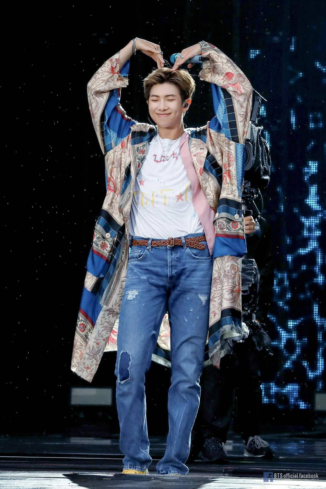 Rm 桌布 壁紙 — 一位微笑的表演者在舞台上用雙手比出愛心，身穿彩色圖案外套和破洞牛仔褲。