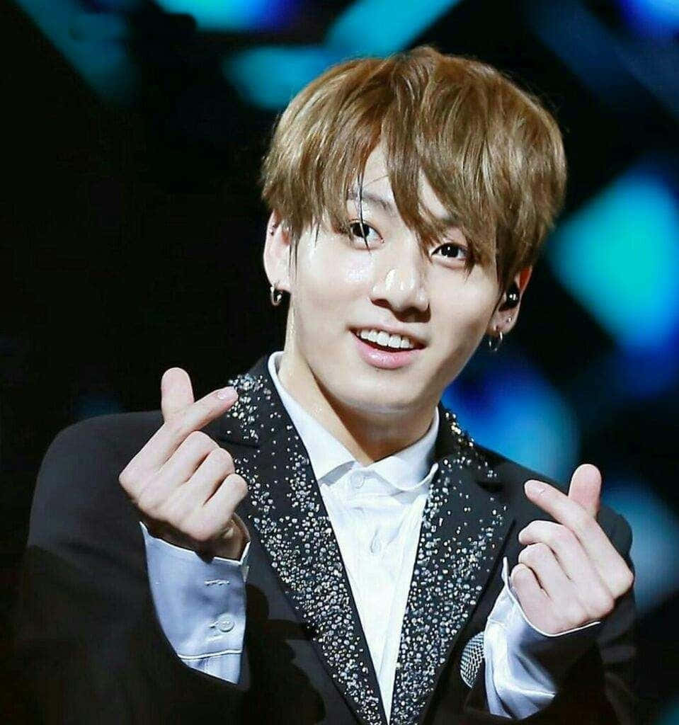 BTS 桌布 壁紙 — 一位微笑的表演者穿著閃亮黑色西裝，在藍色舞台燈光下做出心形手勢。