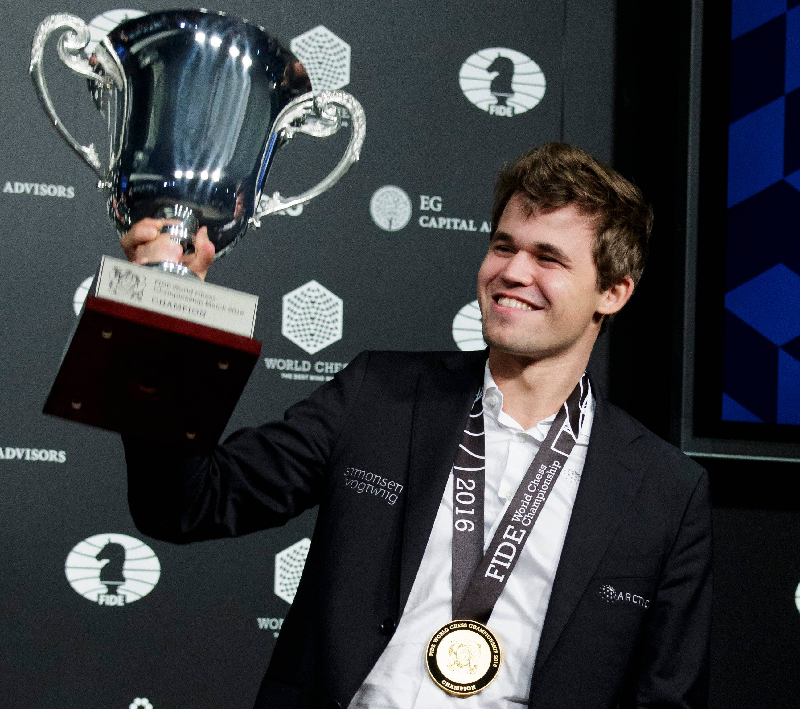 Magnus 桌布 壁紙 — 一位微笑的西洋棋冠軍在正式活動中自豪地拿著一個大銀獎盃，並佩戴著冠軍獎牌。