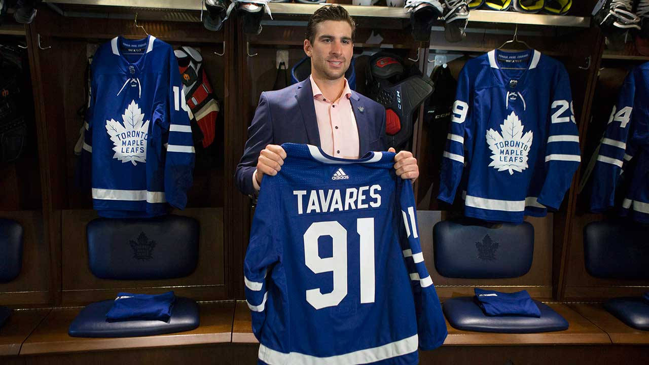 運動 桌布 壁紙 — 一位微笑的西裝男子在木製更衣室中舉起一件印有Tavares 91的多倫多楓葉隊球衣。
