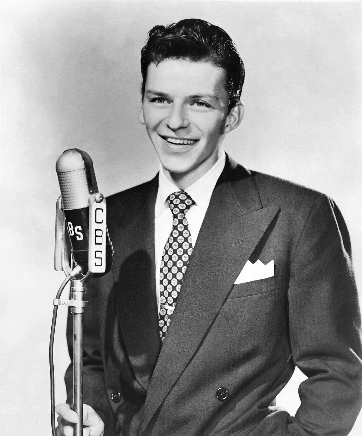 Sinatra 桌布 壁紙 — 一位微笑的西裝男子站在經典工作室肖像中的復古CBS麥克風旁。
