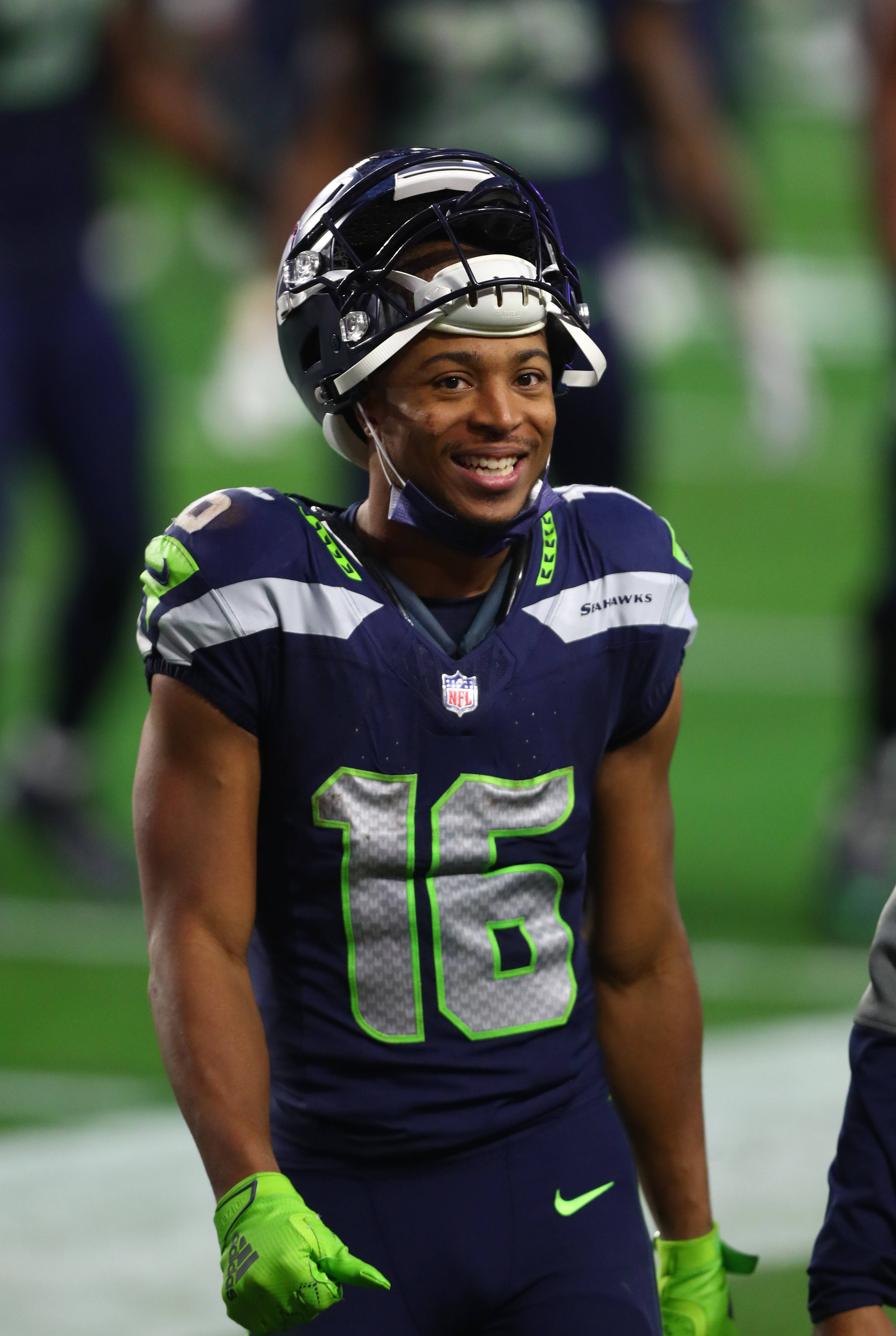 Seattle Seahawks 桌布 壁紙 — 一位微笑的西雅圖海鷹隊美式足球員，身穿16號球衣和頭盔，在綠色球場上，球場燈光下。