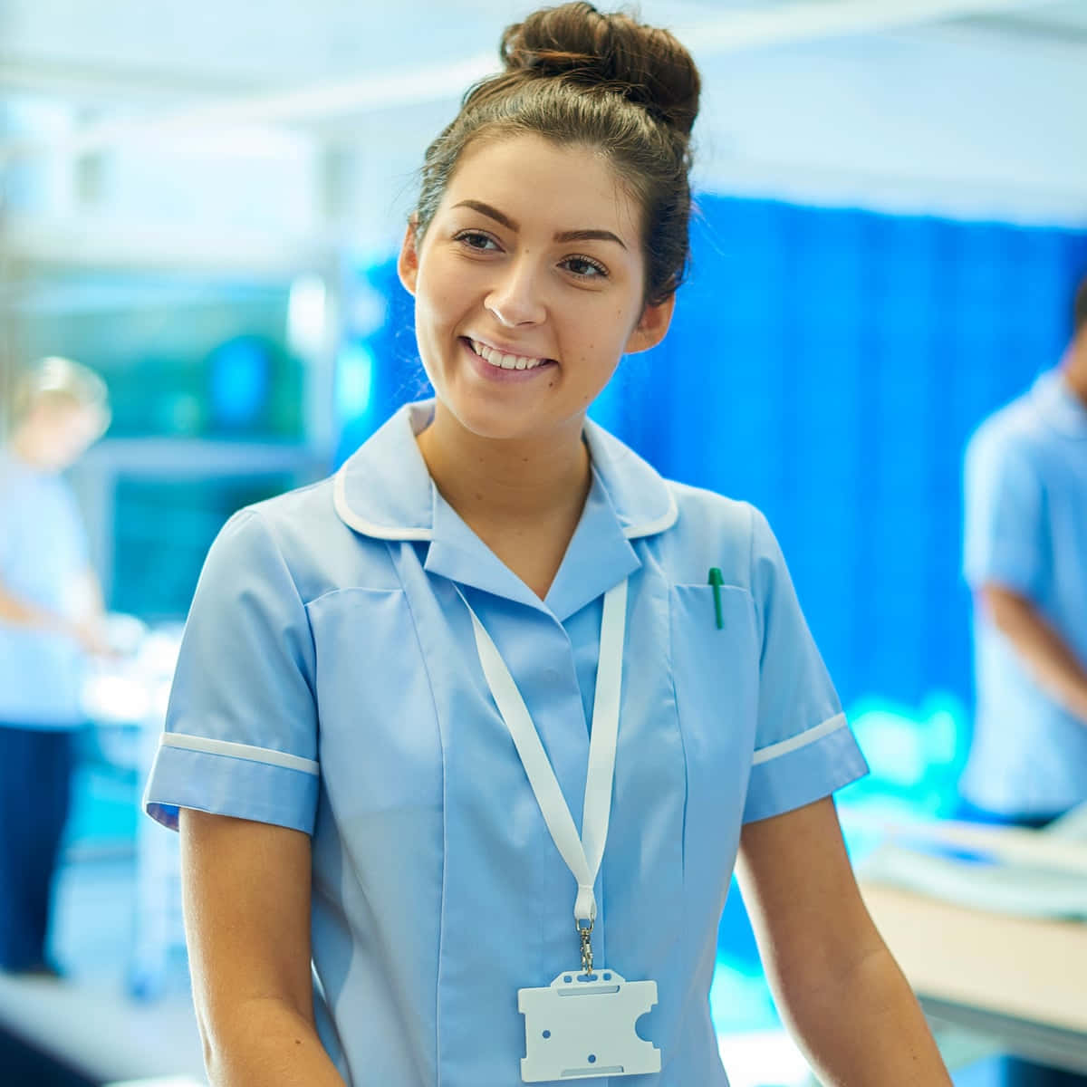 Nursing 桌布 壁紙 — 一位微笑的護士穿著淺藍色白色飾邊制服，自信地站在明亮的醫院走廊。