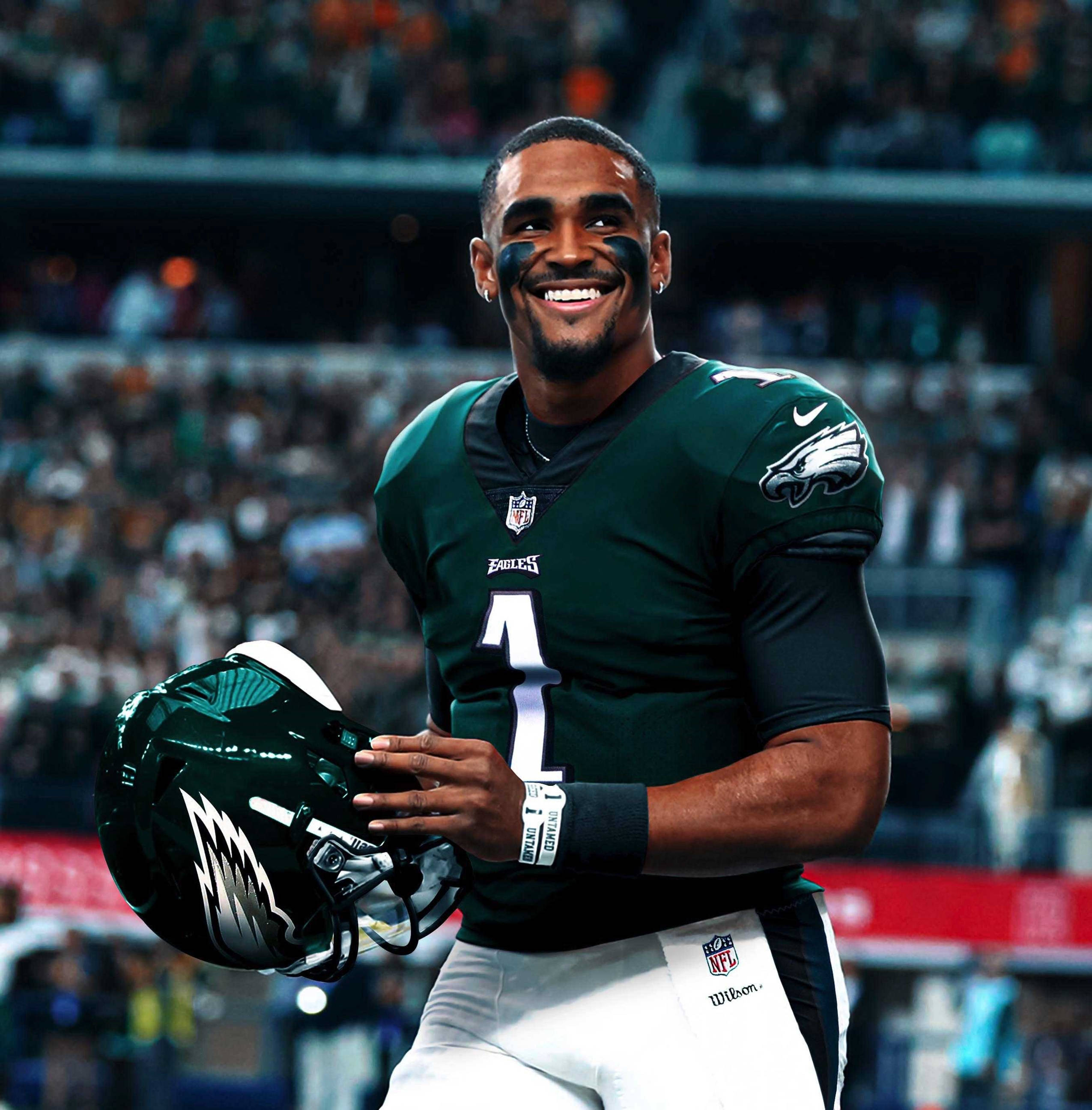 Jalen Hurts Eagles 桌布 壁紙 — 一位微笑的費城老鷹隊四分衛身穿綠色球衣，在球場燈光下拿著頭盔慶祝。