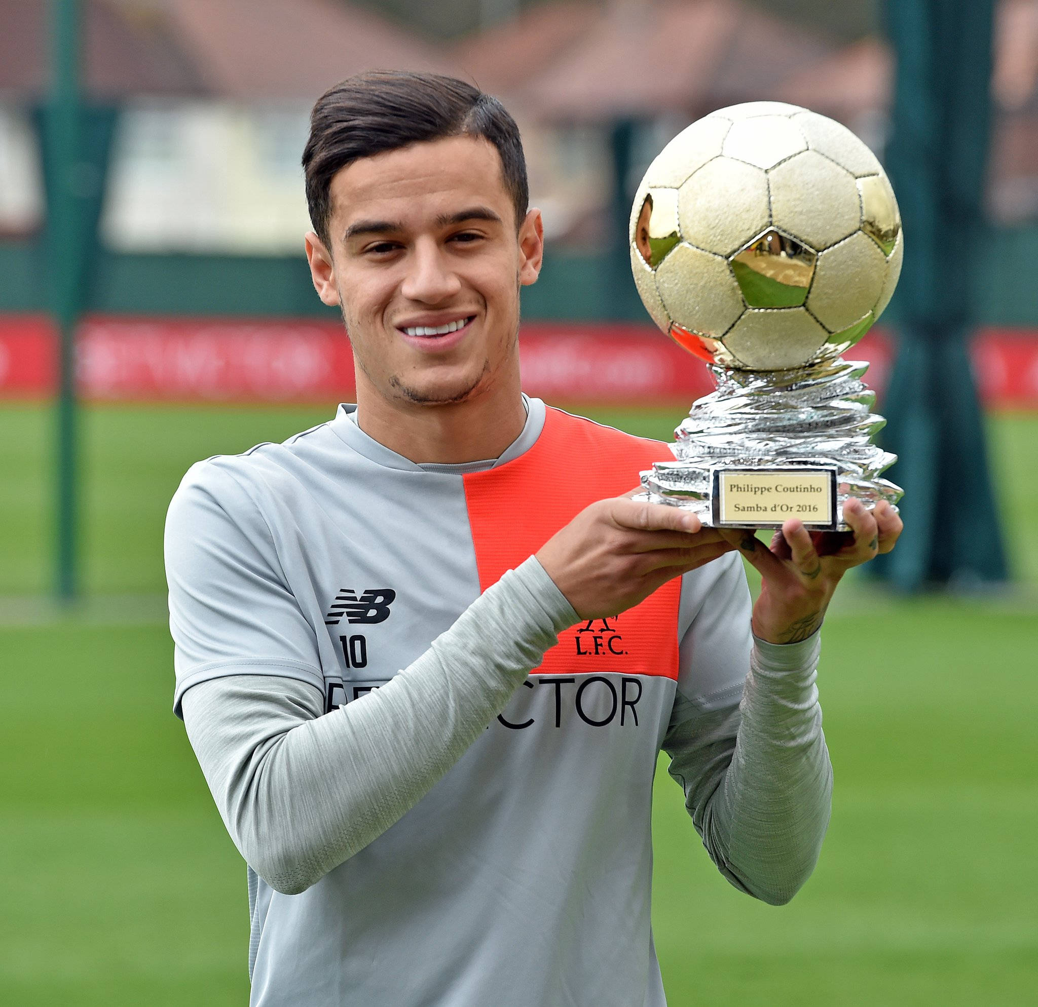 Coutinho 桌布 壁紙 — 一位微笑的足球員穿著訓練服，在草地上自豪地舉起一個金色的足球獎盃。
