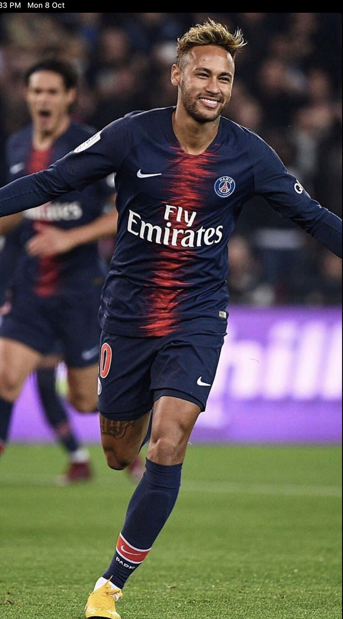 Neymar iPhone 桌布 壁紙 — 一位微笑的足球員身穿巴黎聖日耳曼球衣，在球場燈光下於充滿活力的綠色草地上慶祝進球。