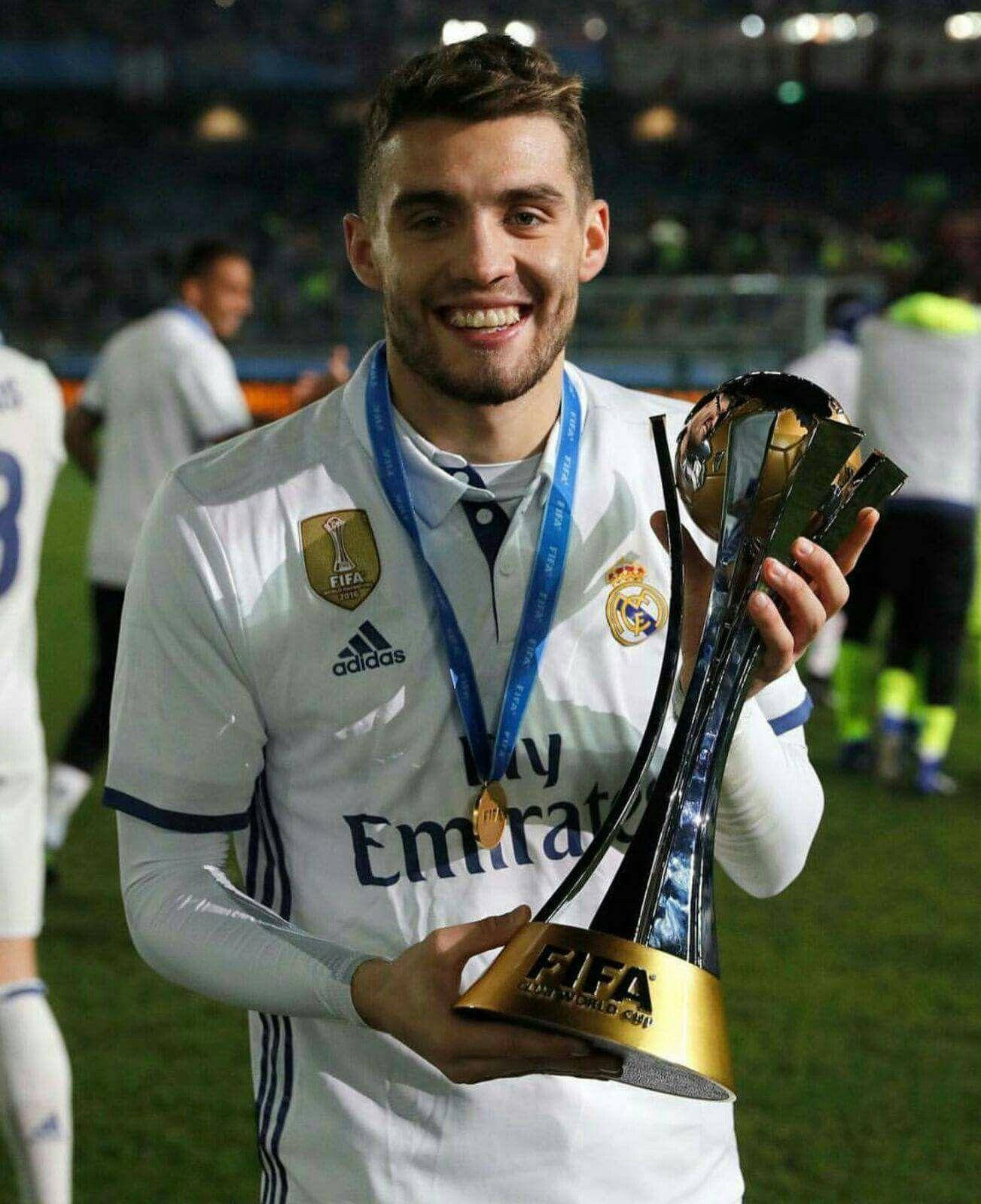 Football Players 桌布 壁紙 — 一位微笑的足球員身穿白色皇家馬德里球衣，在夜晚的球場上自豪地舉起閃亮的FIFA世界冠軍球會盃獎盃。