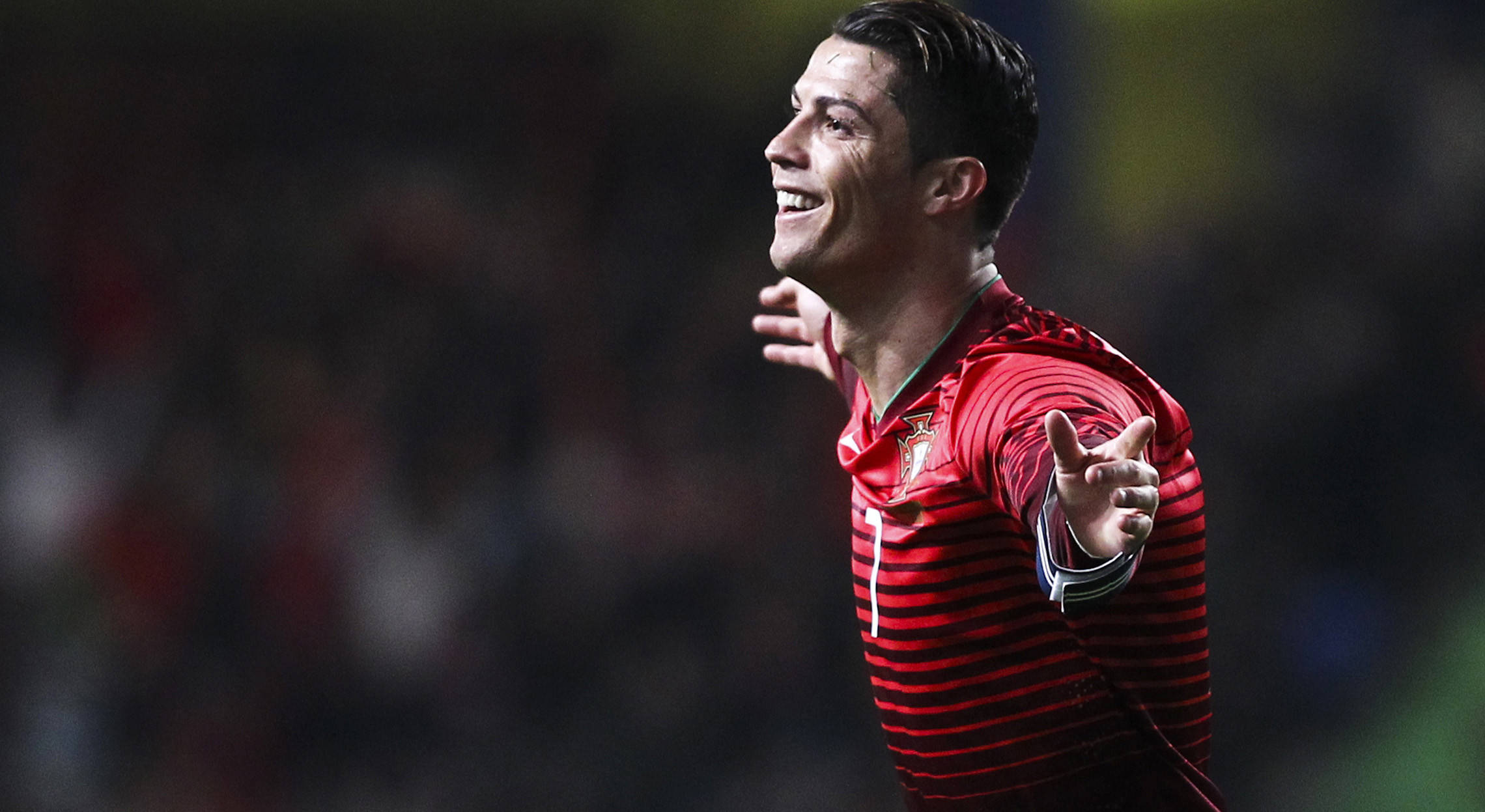 Cr7 桌布 壁紙 — 一位微笑的足球員身穿紅色條紋球衣，在模糊的體育場人群中張開雙臂慶祝。
