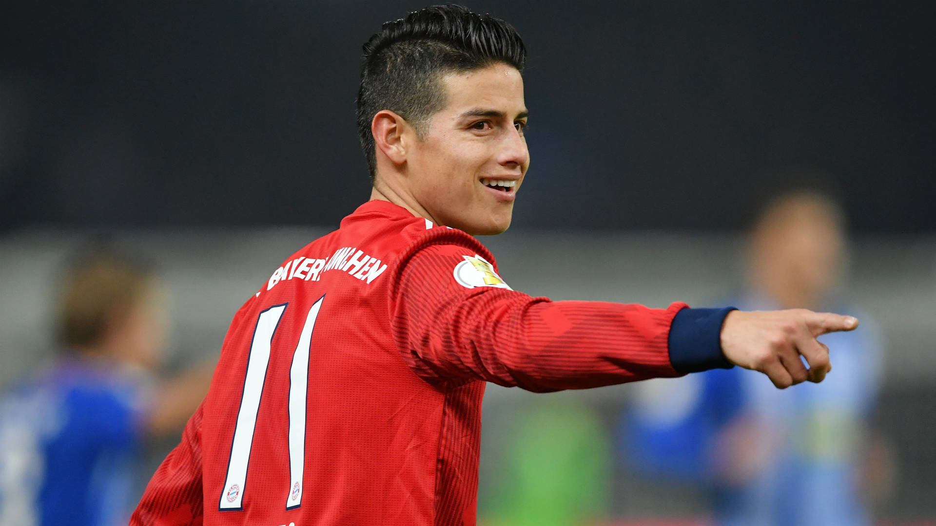 James Rodriguez 桌布 壁紙 — 一位微笑的足球員身穿紅色球衣，背號11，在球場燈光下比賽時向前指。