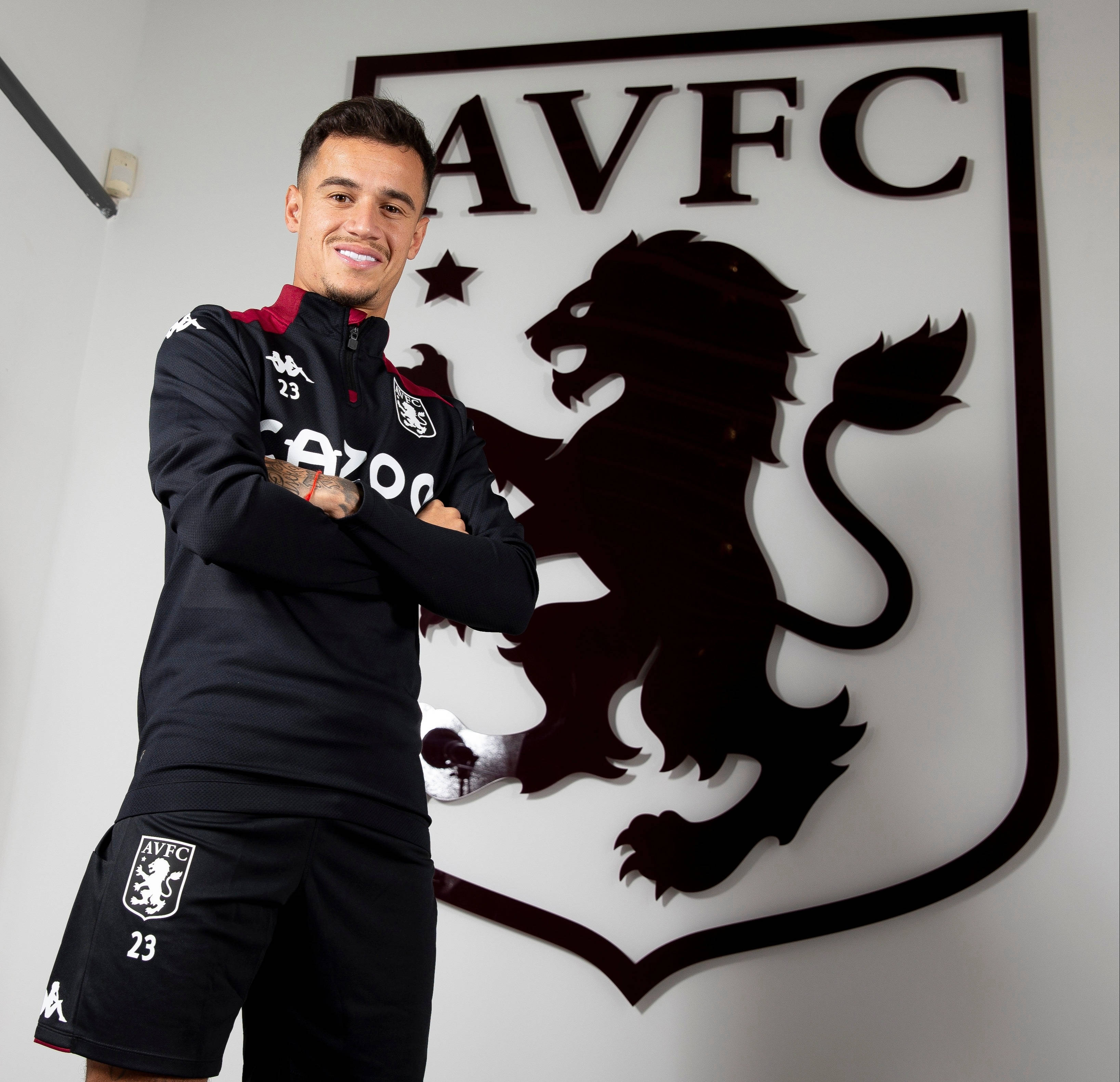 Coutinho 桌布 壁紙 — 一位微笑的足球員身穿阿斯頓維拉球衣，自信地交叉雙臂站在球會大型獅子徽章前。