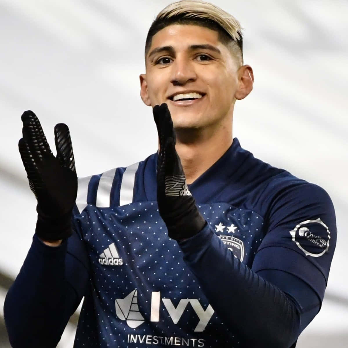 Soccer Aesthetic 桌布 壁紙 — 一位微笑的足球運動員身穿帶有白色圓點的深藍色球衣和黑色手套，在模糊的體育場背景下拍手。