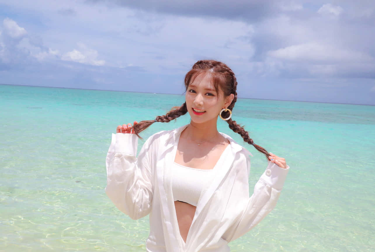 twice 桌布 壁紙 — 一位微笑的辮子女性在部分多雲的天空下，在碧綠海洋的邊緣頑皮地握著她的辮子。