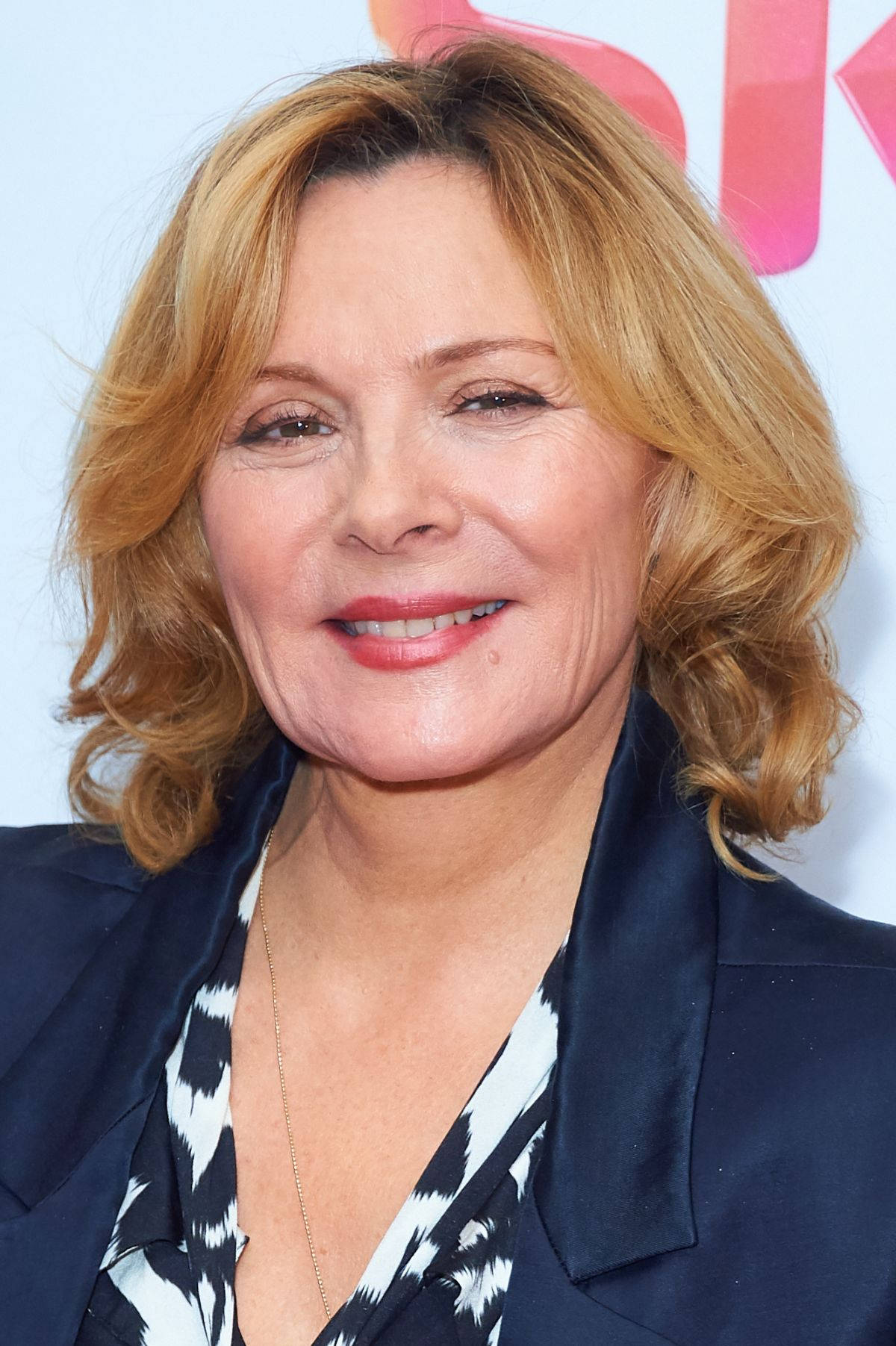 Celebrity 桌布 壁紙 — 一位微笑的金色波浪長髮女性近距離肖像，身穿海軍藍西裝外套，內搭黑白圖案上衣。