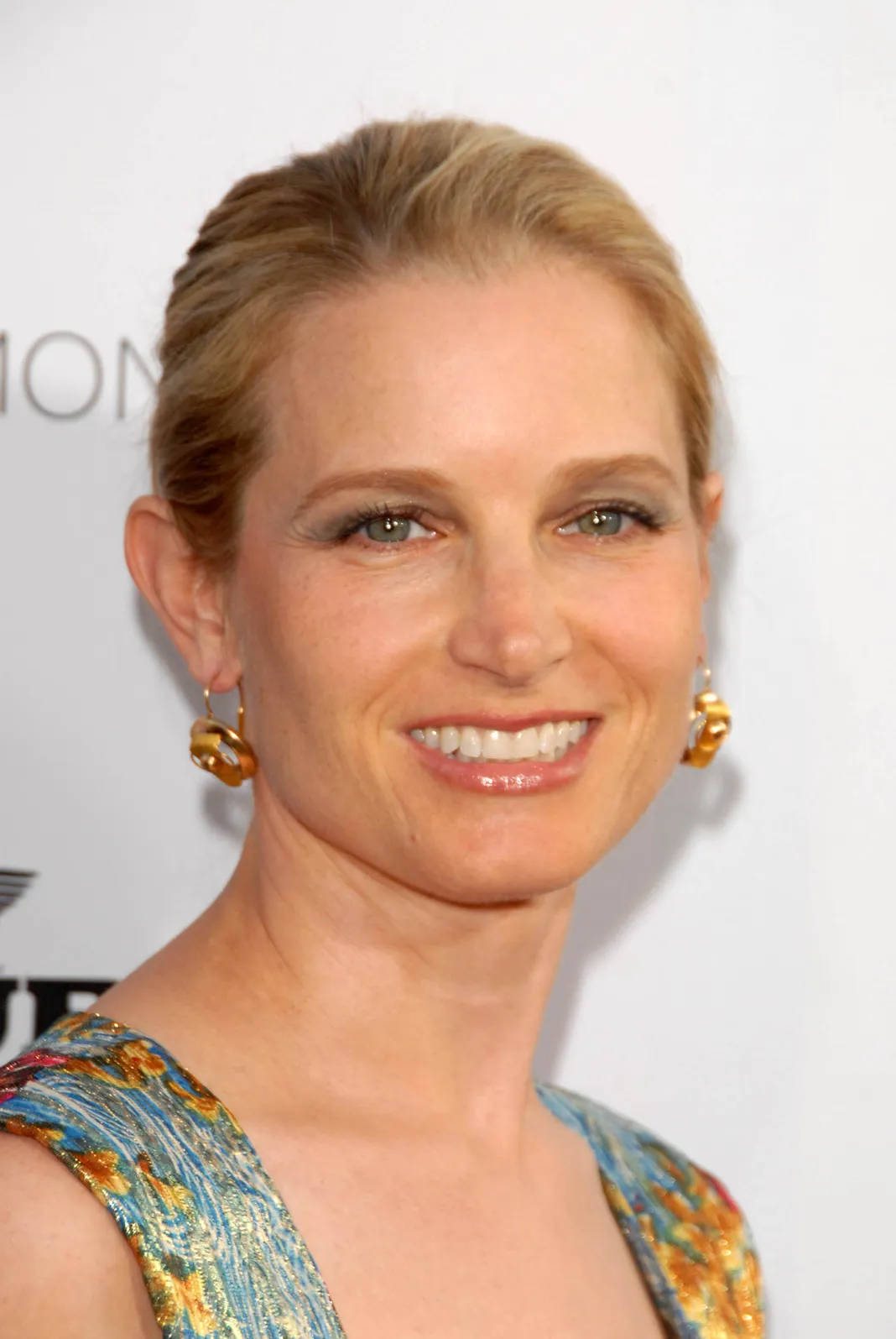 Celebrity 桌布 壁紙 — 一位微笑的金髮女子戴著金色耳環，身穿色彩繽紛的圖案連衣裙，背景為白色。