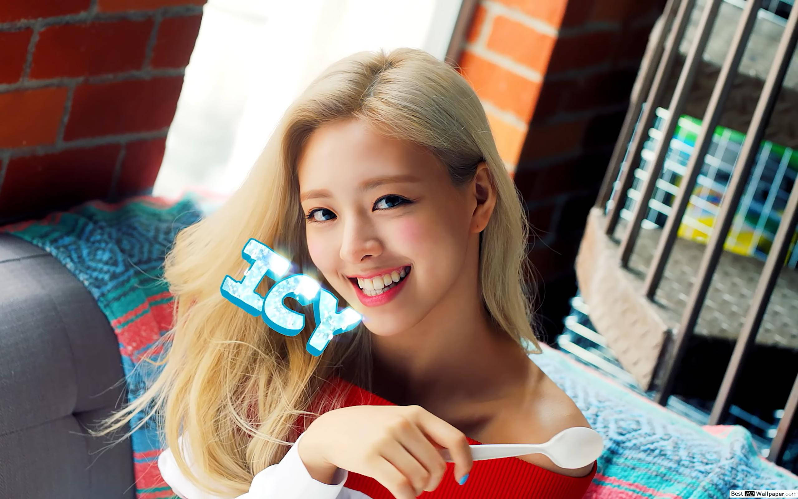 ITZY 桌布 壁紙 — 一位微笑的金髮女子拿著湯匙，在磚牆和彩色毯子前展示一個冰冷的圖案。